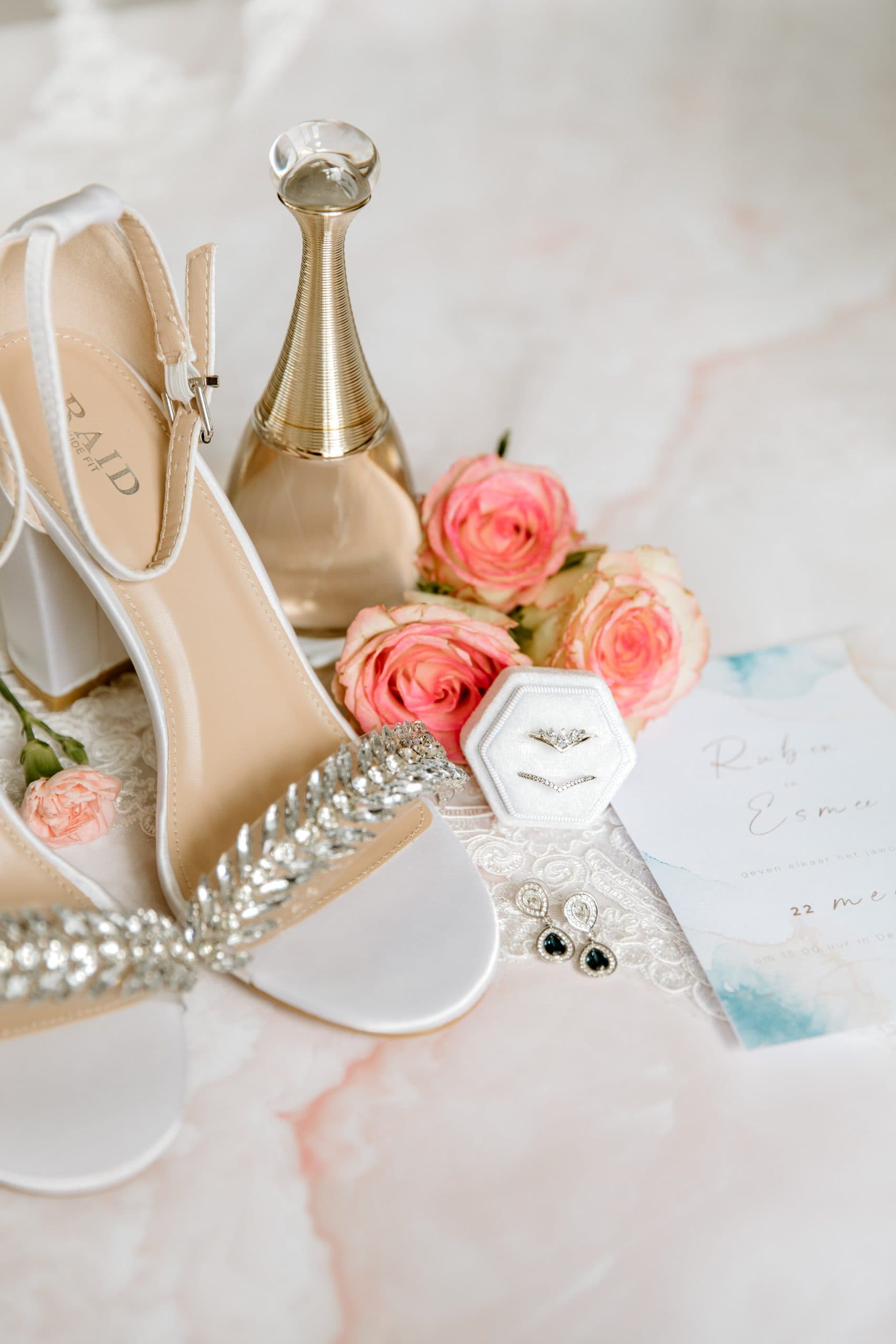 Witte trouwschoenen en sieraden op een marmeren tafel voor detailfotografie op de bruiloft.