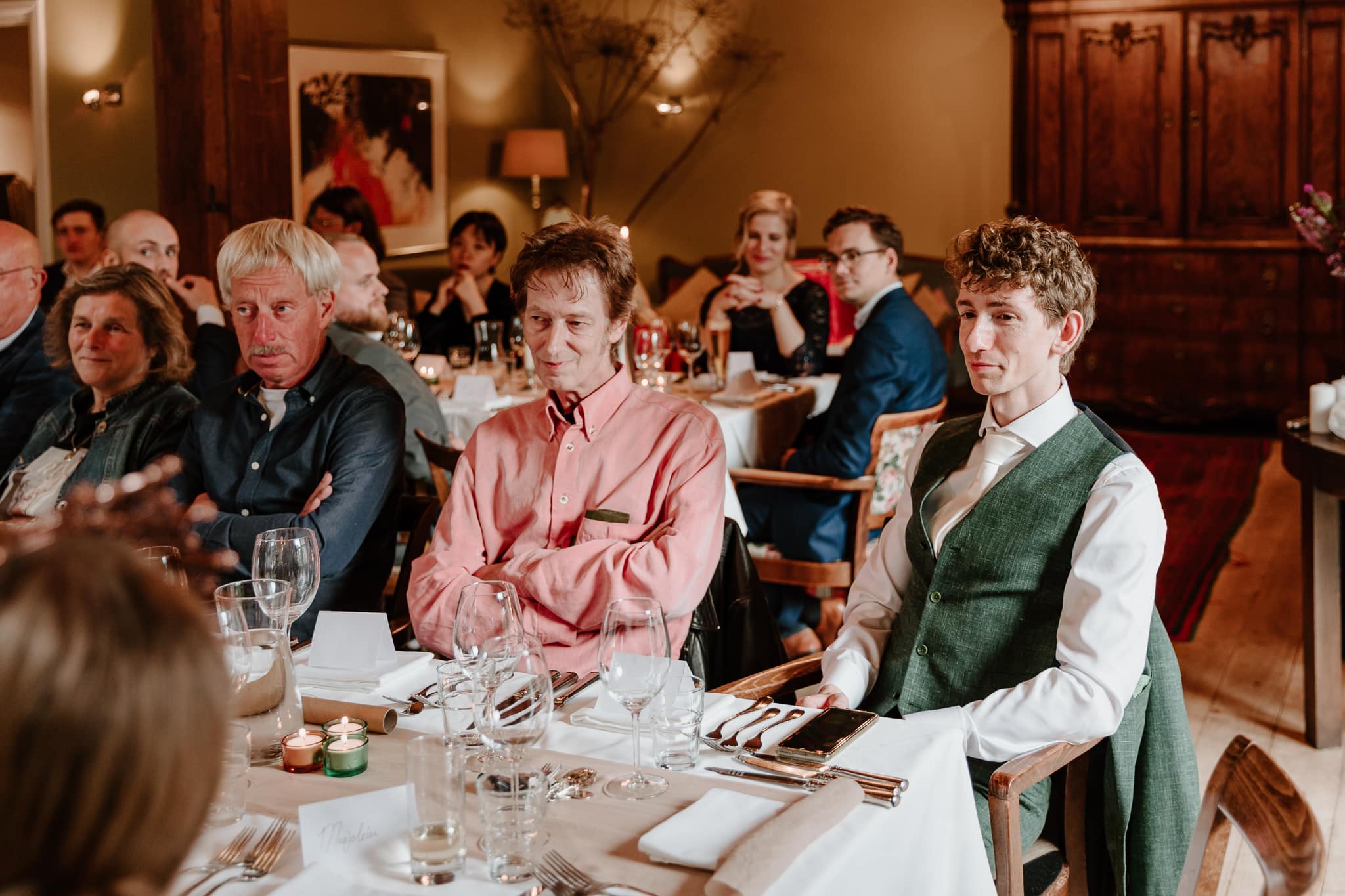 De bruidegom zit naast zijn vader en kijkt liefdevol naar zijn bruid tegenover hem tijdens het diner op de bruiloft in Drenthe.