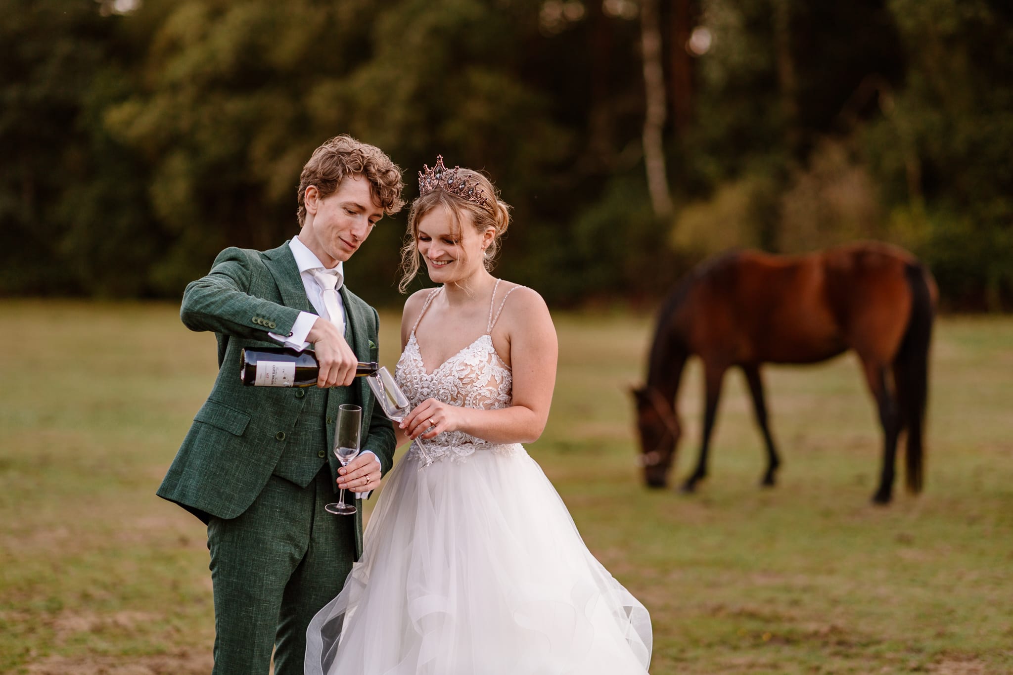 Bruidspaar schenkt na de bruiloft in Drenthe een glas champagne in in weide met op de achtergrond een paard tijdens het maken van foto's door bruidsfotograaf Drenthe Lisan Spiegelaar fotografie.