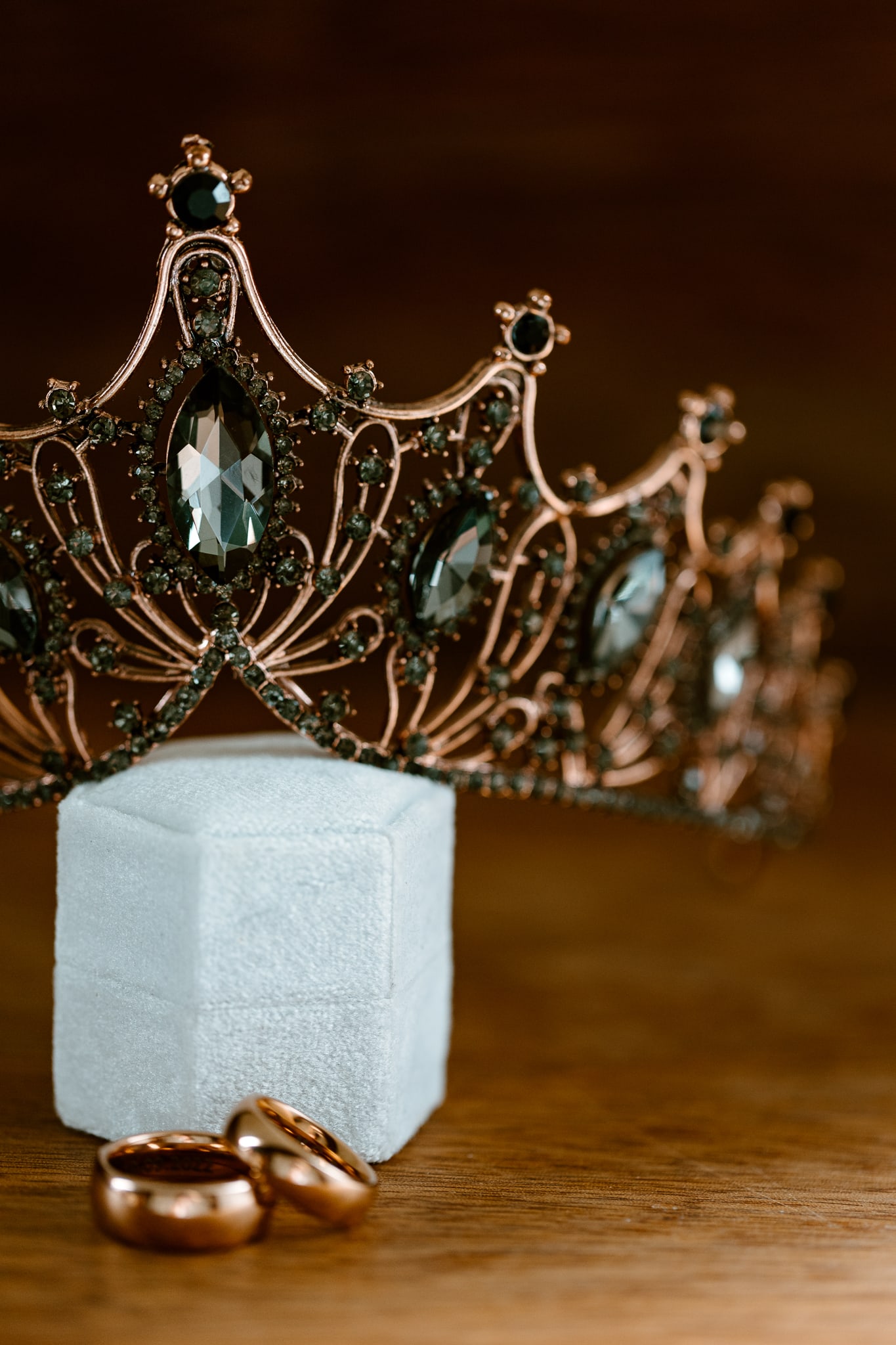 Een tiara met zwarte diamanten leunt op een ringendoosje. Voor het ringendoosje liggen twee trouwringen.