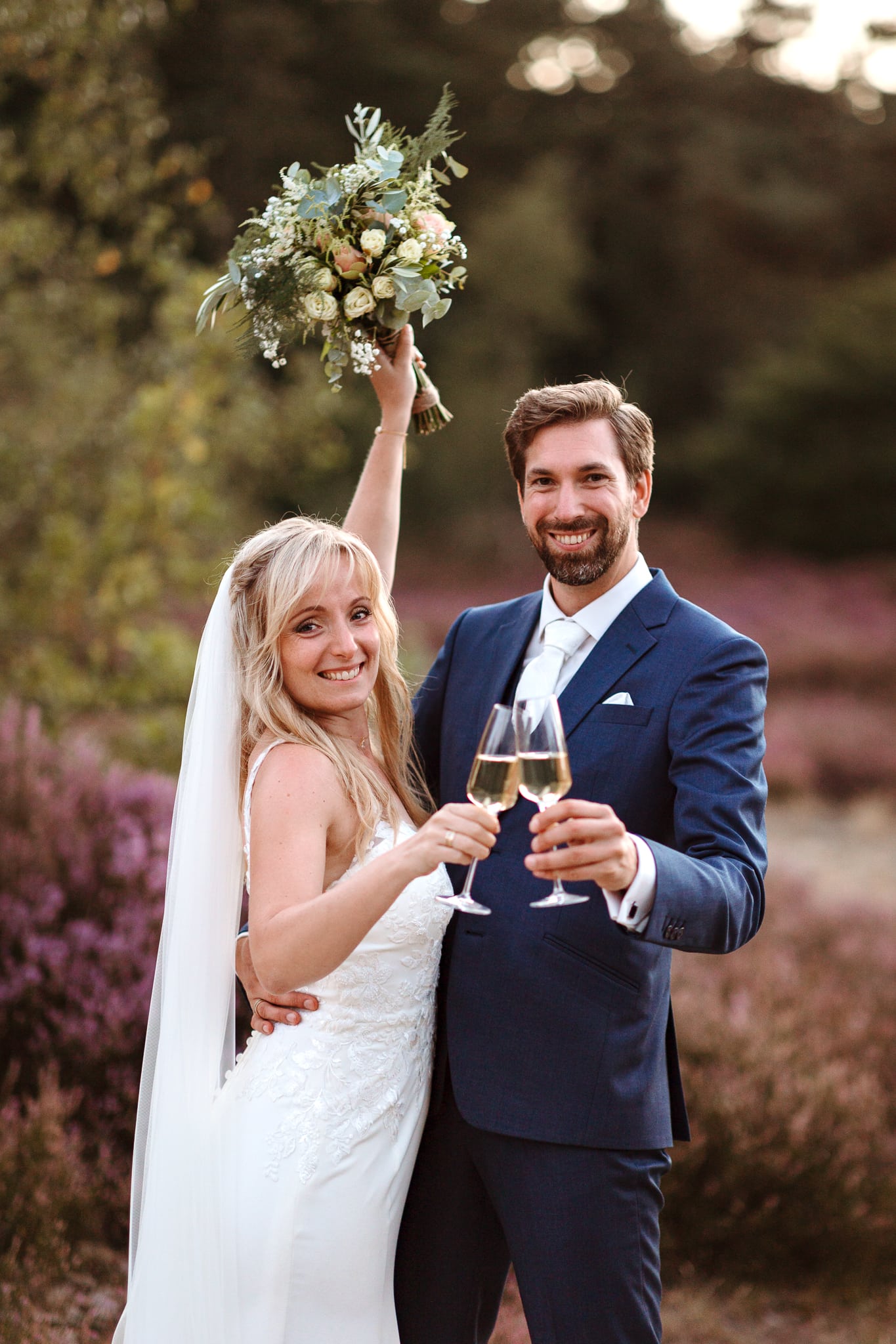 Bruidspaar proost met champagne en de bruid houdt juichend haar boeket in de lucht.