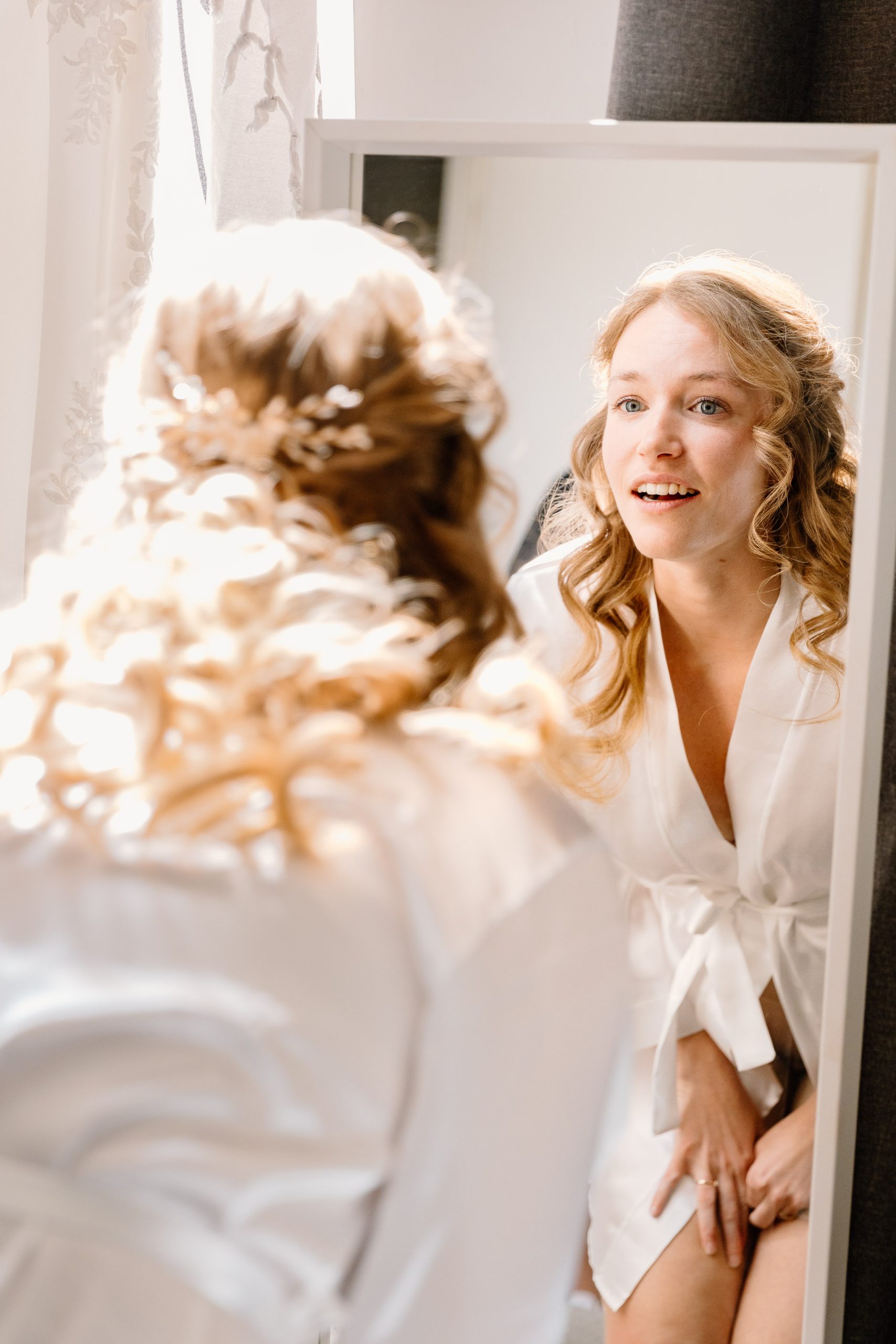 Een bruid in Groningen bewondert haar make-up en haar in de spiegel.