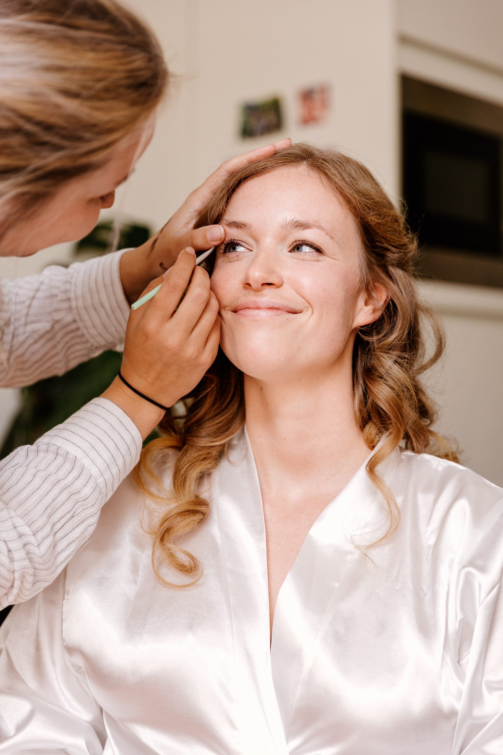 Een bruid lacht naar haar visagist terwijl haar oogmake-up wordt gedaan.