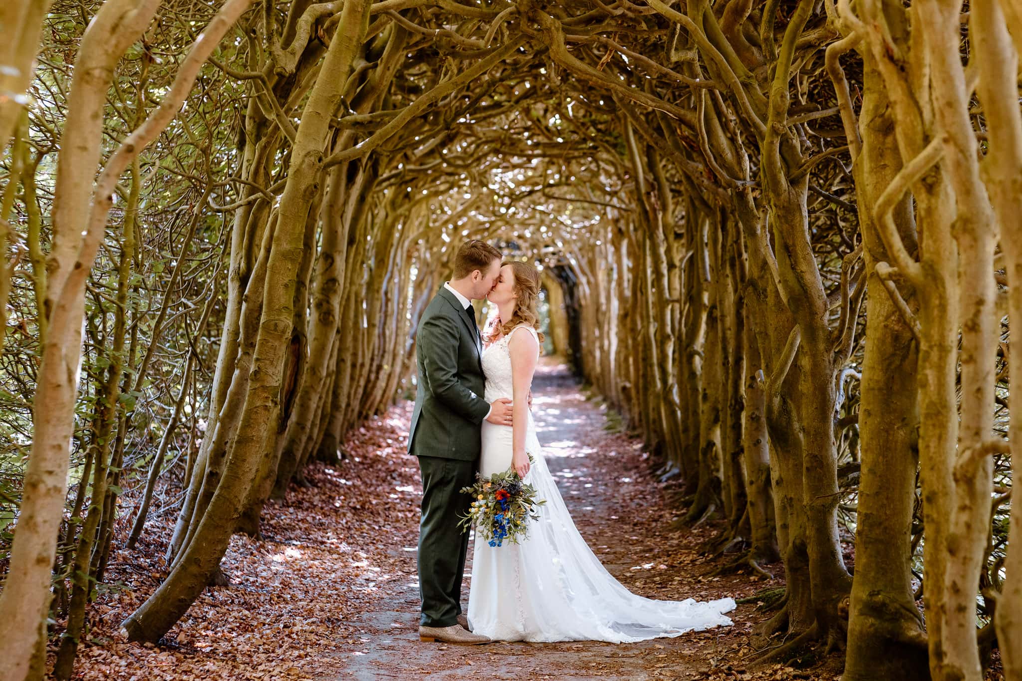 Een bruid en bruidegom kussen elkaar in een tunnel van bomen op een trouwfoto in Landgoed de Braak gemaakt door trouwfotograaf Groningen Lisan Spiegelaar.