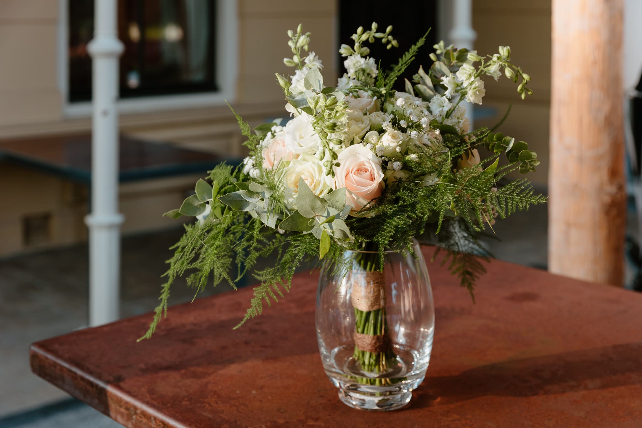 Trouwboeket met witte rozen en varens buiten op een bartafel.