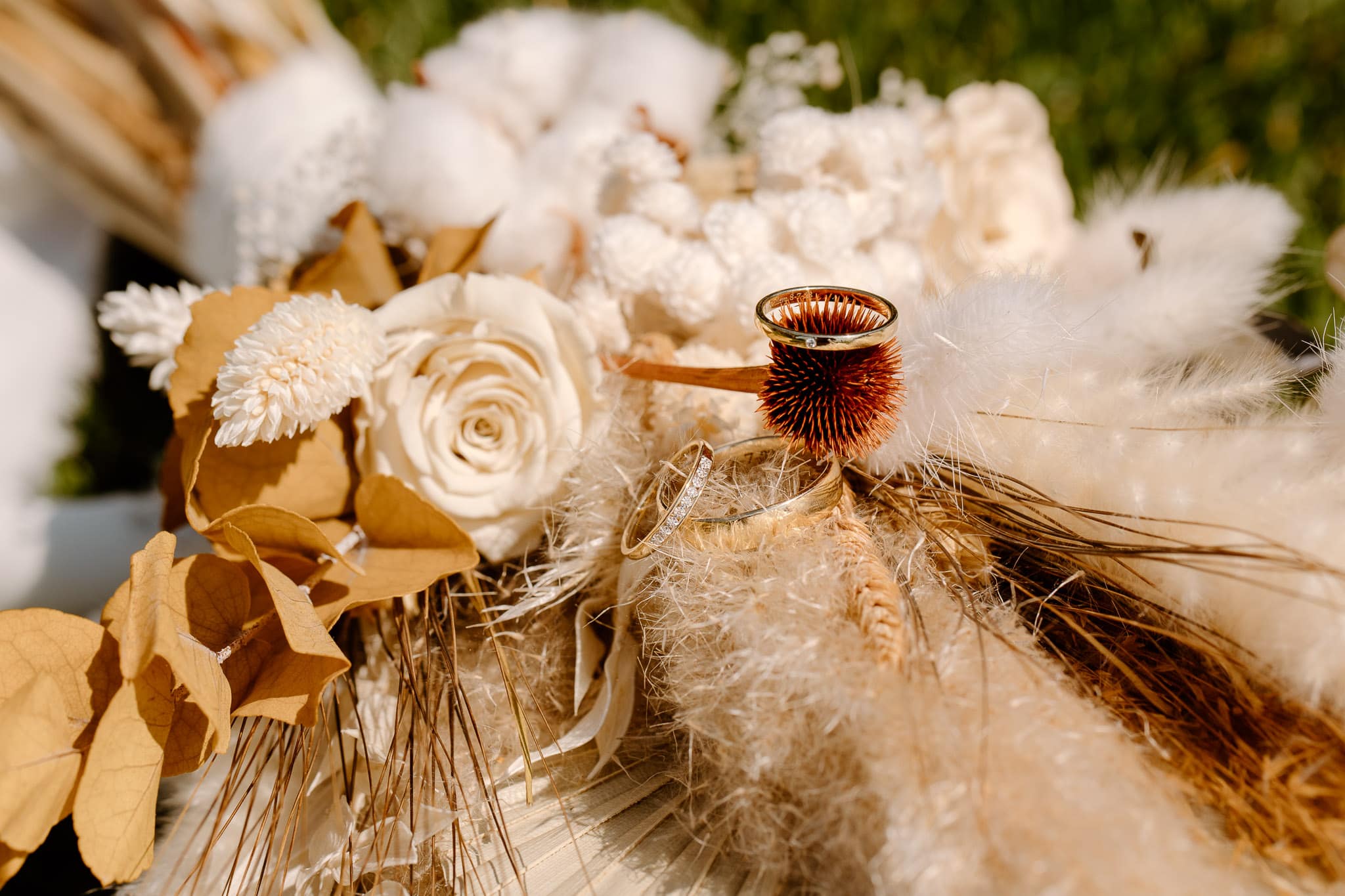 Boho trouwboeket op de zon in het gras met de trouwringen erop voor de detailfoto's.