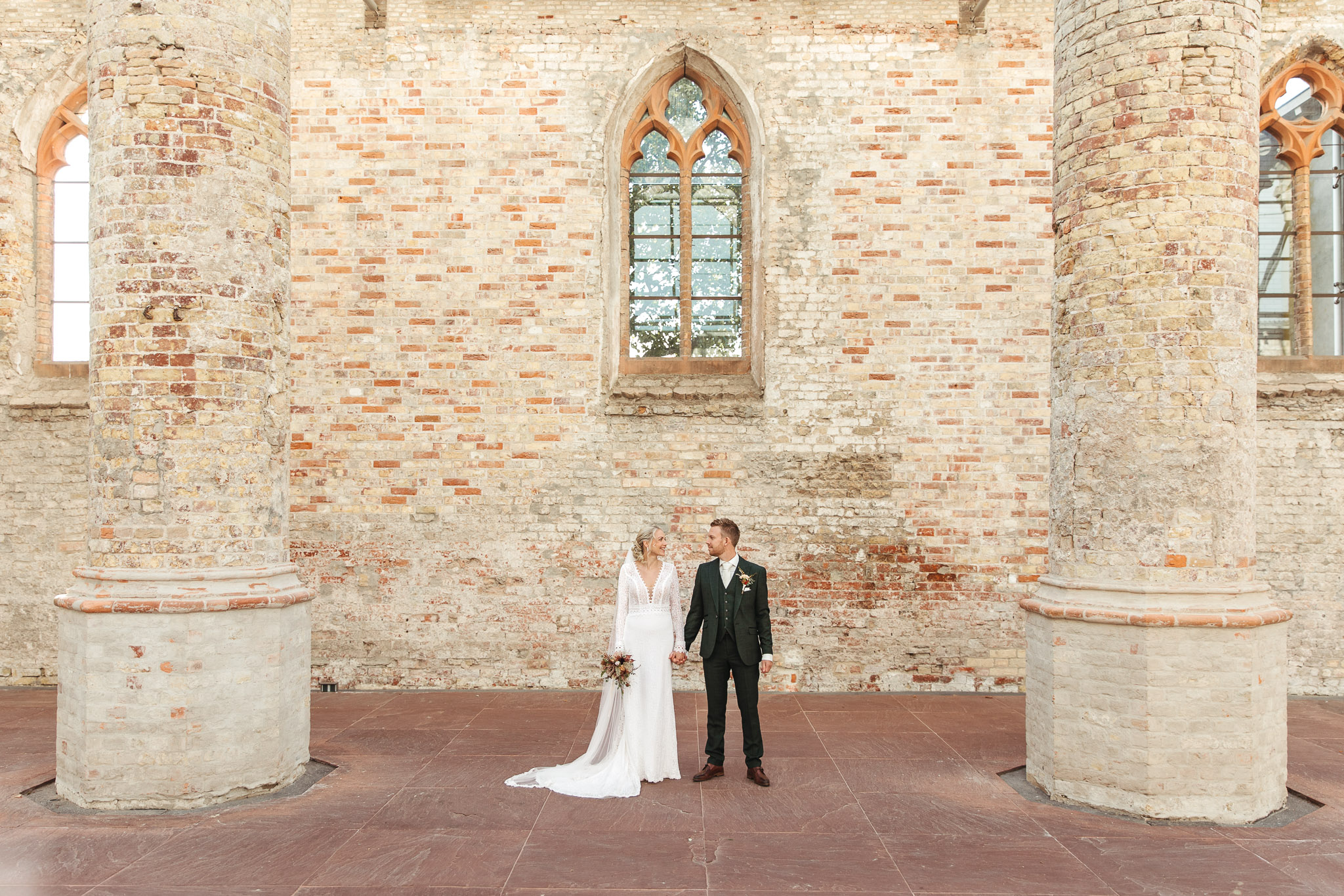 Een bruid en bruidegom staan hand in hand in een oude kerk tijdens hun fotoshoot