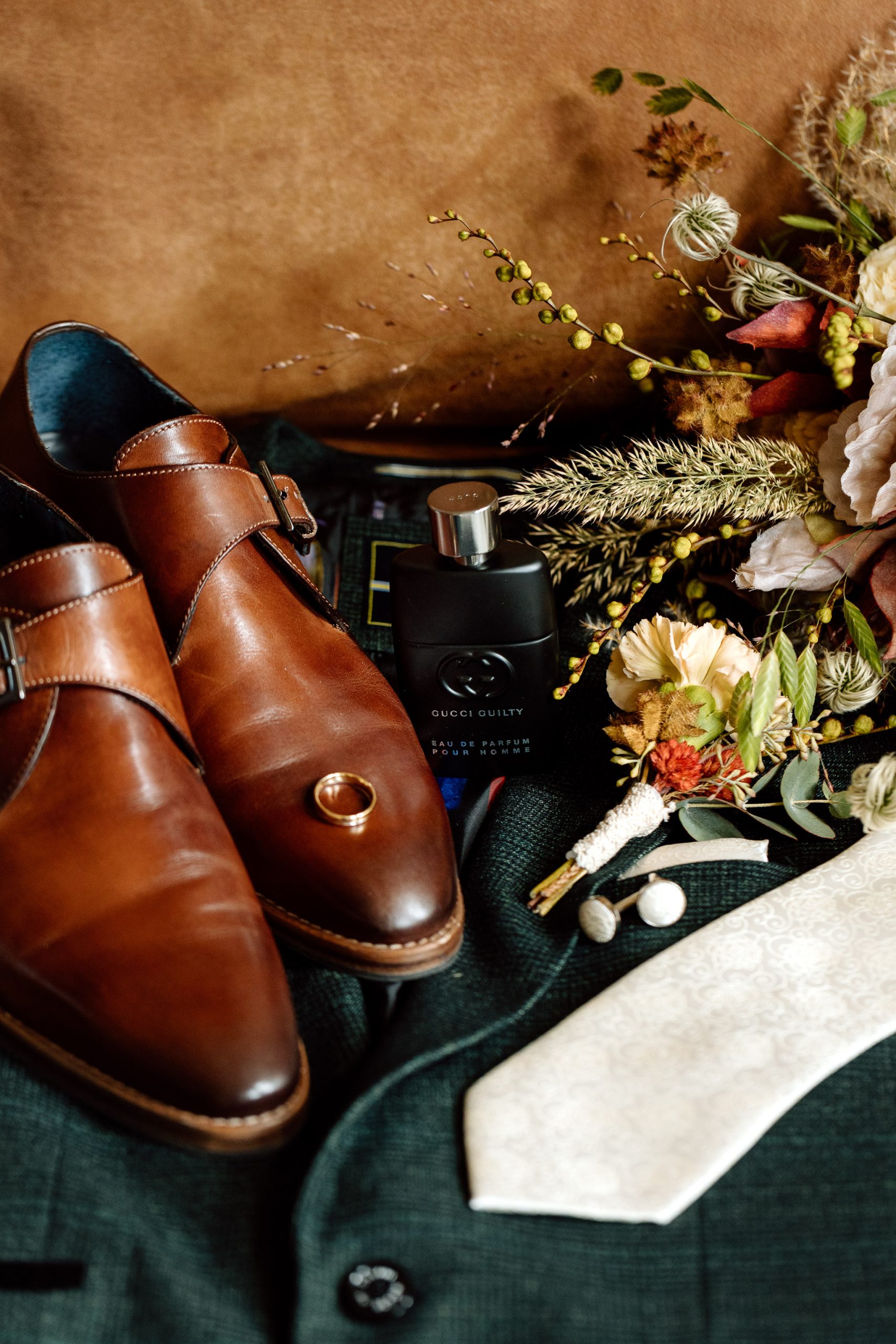 Een paar bruine trouwschoenen, een een flesje parfum, het trouwboeket en de stropdas op het trouwcolbert van een Friese bruidegom.