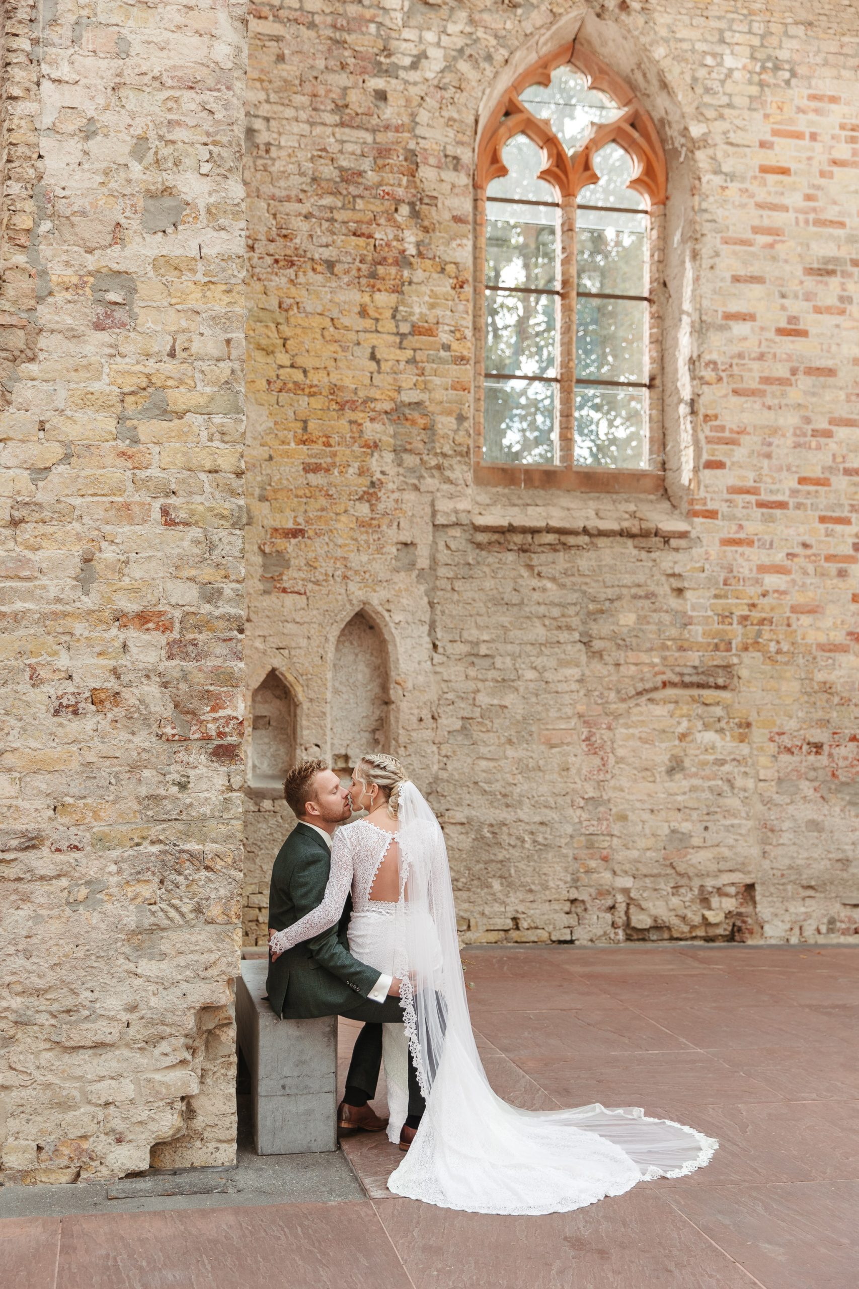 Een bruid en bruidegom kussend in een oud pand, vastgelegd door een vakkundige bruidsfotograaf Fryslân.