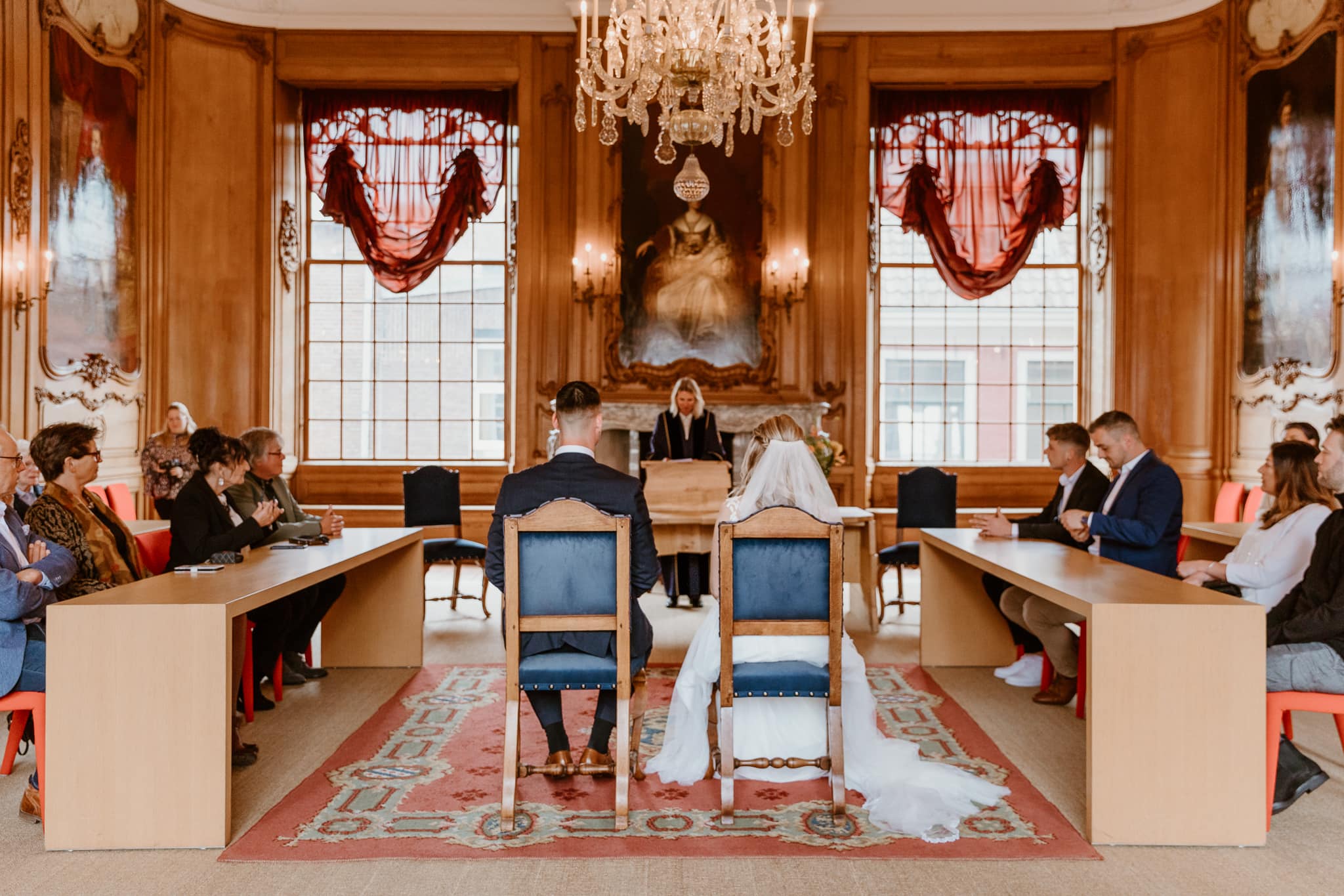 Bruidspaar zit in de historische trouwzaal in het stadhuis van Leeuwarden en wordt van achteren gefotografeerd.