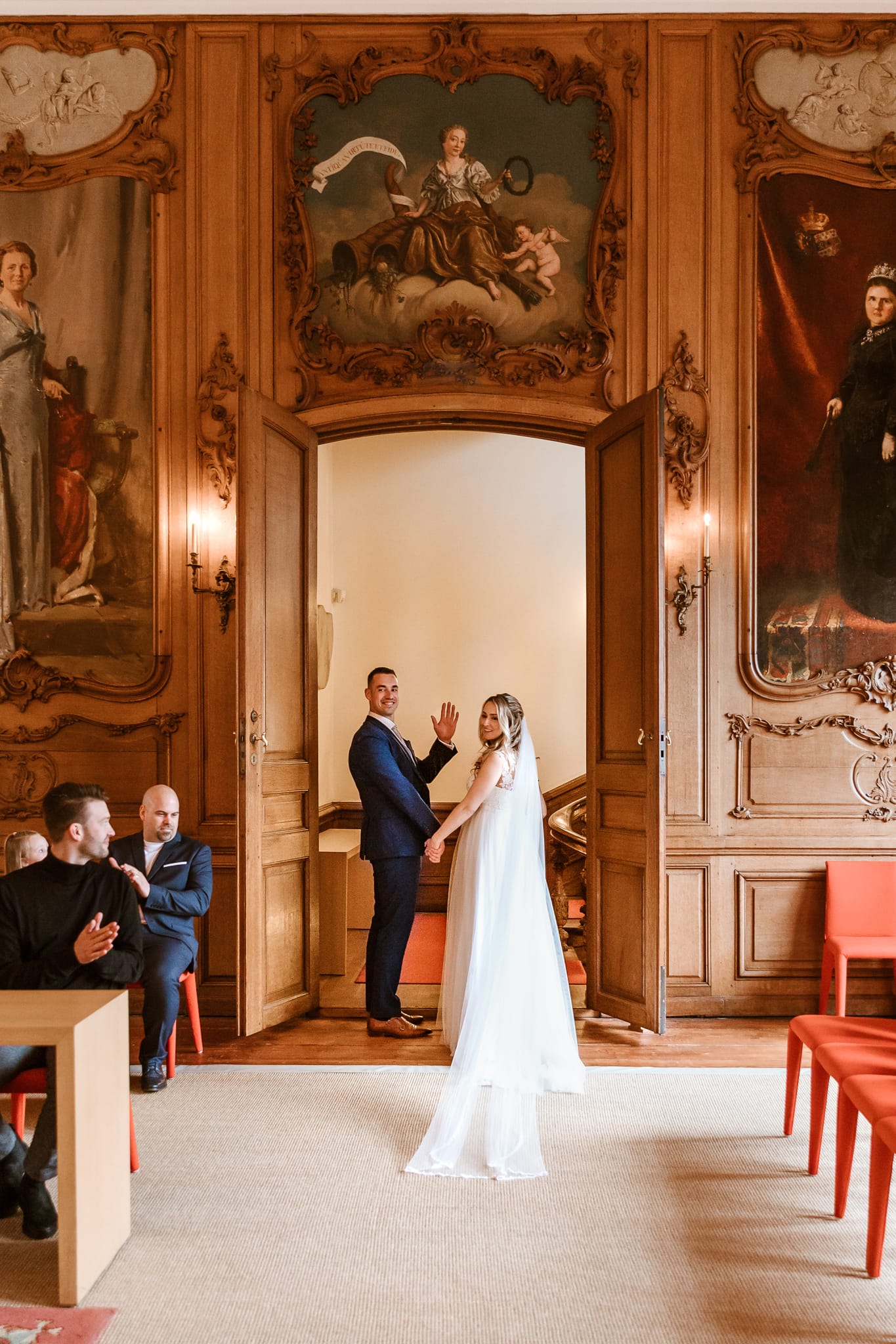 Bruidspaar kijkt achterom en zwaait naar de camera van trouwfotograaf Friesland Lisan Spiegelaar voordat ze de trouwzaal verlaten.