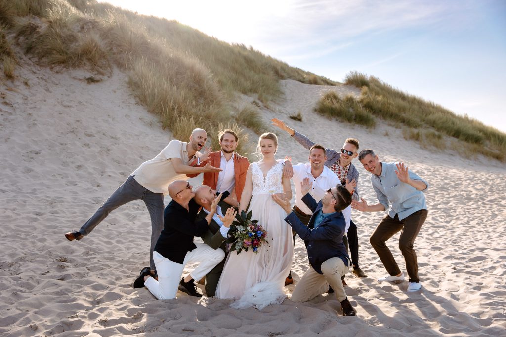 Een groep mensen poseert voor een strandfoto tijdens een trouwstrand Vlieland.