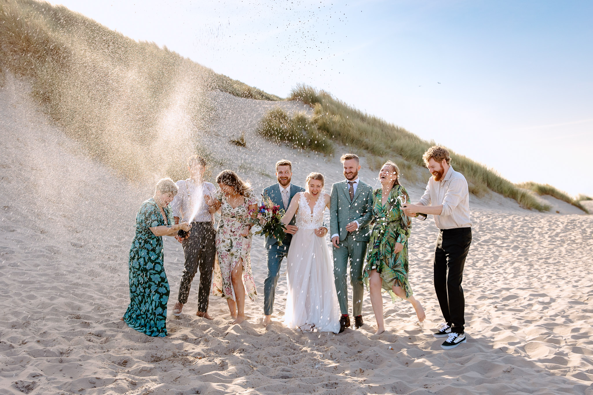 Een groep huwelijksfeesten gooit zand op het strandbruiloft Vlieland strand.