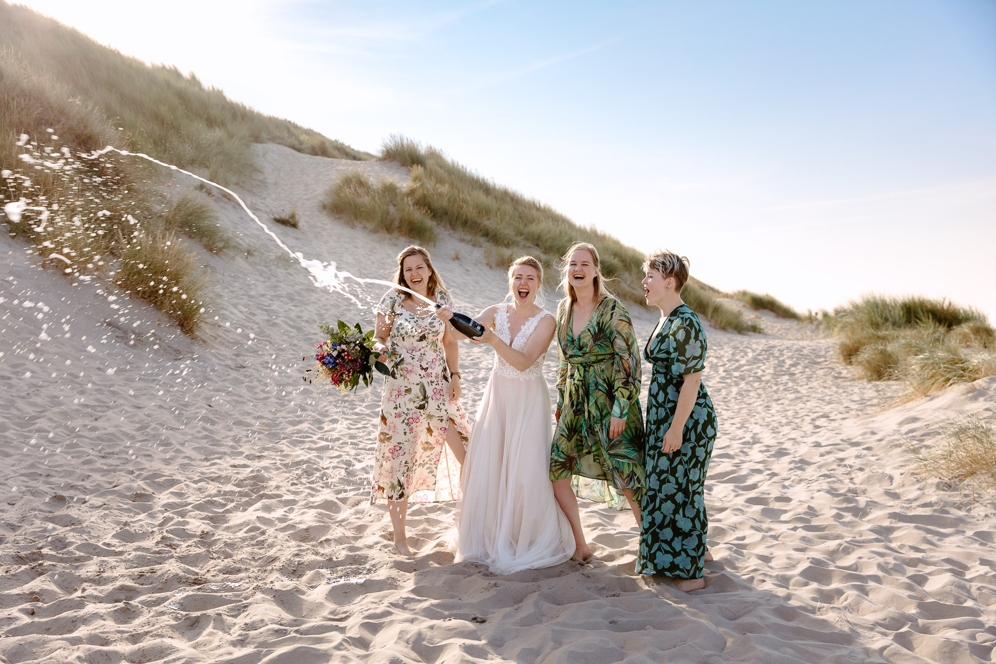 Een groep bruidsmeisjes viert feest met champagne op het zandstrand tijdens een strandbruiloft op Vlieland.