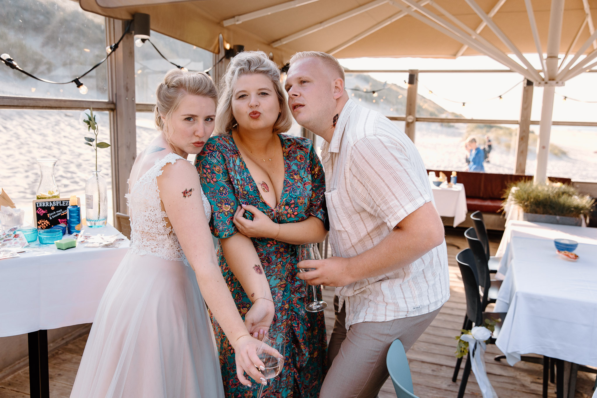 Een groep mensen poseert voor een foto bij een strandrestaurant tijdens een huwelijksceremonie aan de pittoreske oever van Vlieland.