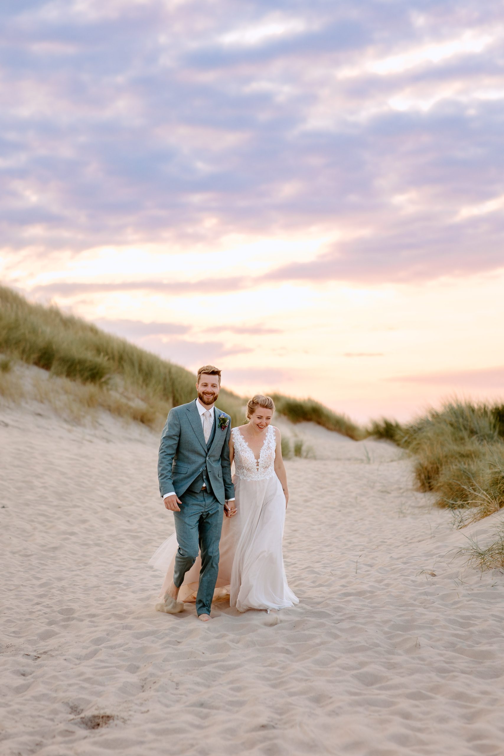 Een bruid en bruidegom die een romantische strandhuwelijksceremonie hebben bij zonsondergang op de prachtige zandduinen van Vlieland.