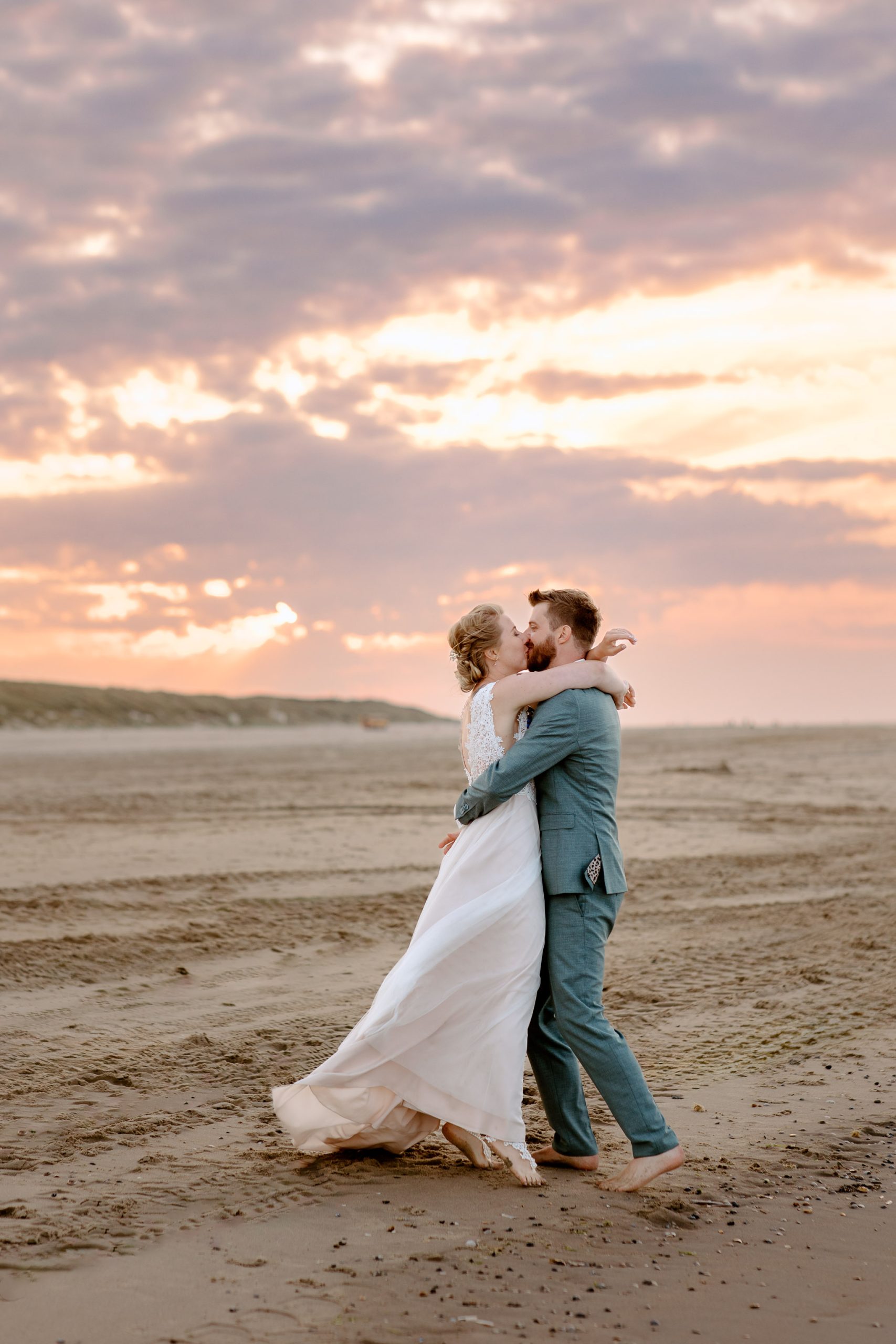 Een strandbruiloft op Vlieland, waarbij het bruidspaar elkaar omhelst terwijl de zon ondergaat.