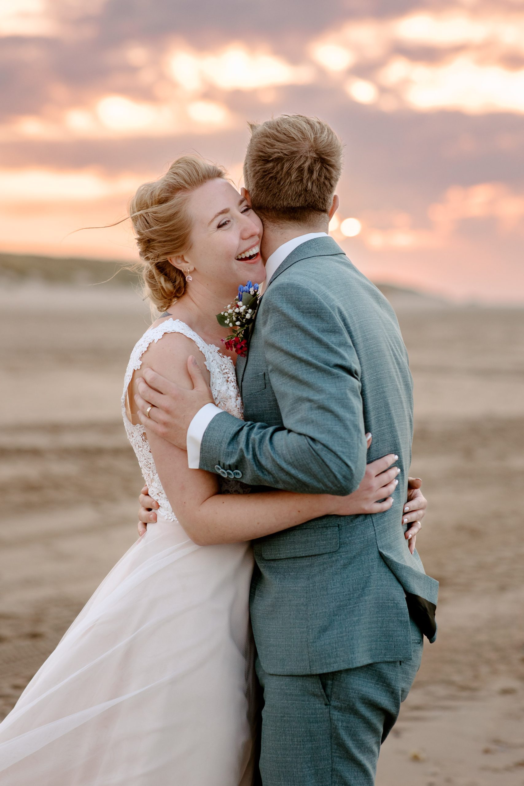 Een bruid en bruidegom omhelzen elkaar op het strand bij zonsondergang tijdens hun strandbruiloft Vlieland.