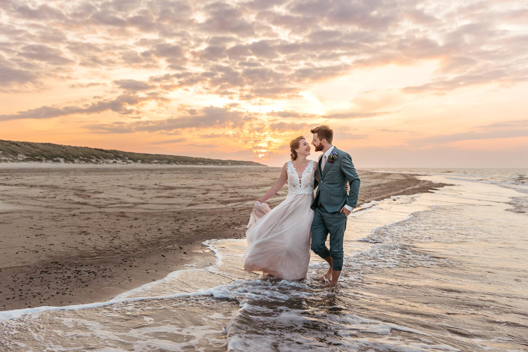 Trouwen op Vlieland, een bruid en bruidegom die bij zonsondergang op het strand staan.