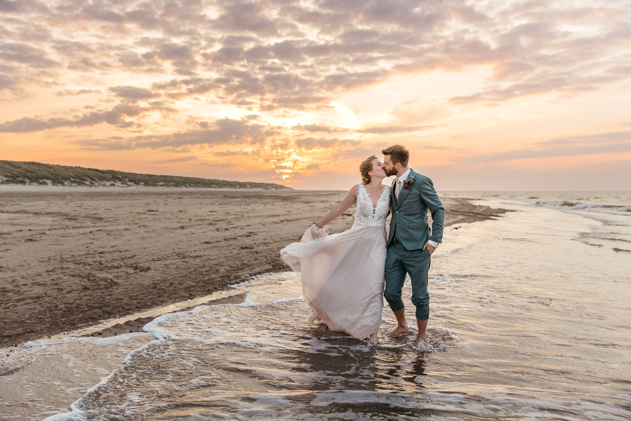 Een koppel zoent op het strand bij zonsondergang tijdens hun romantische huwelijksceremonie op Vlieland.