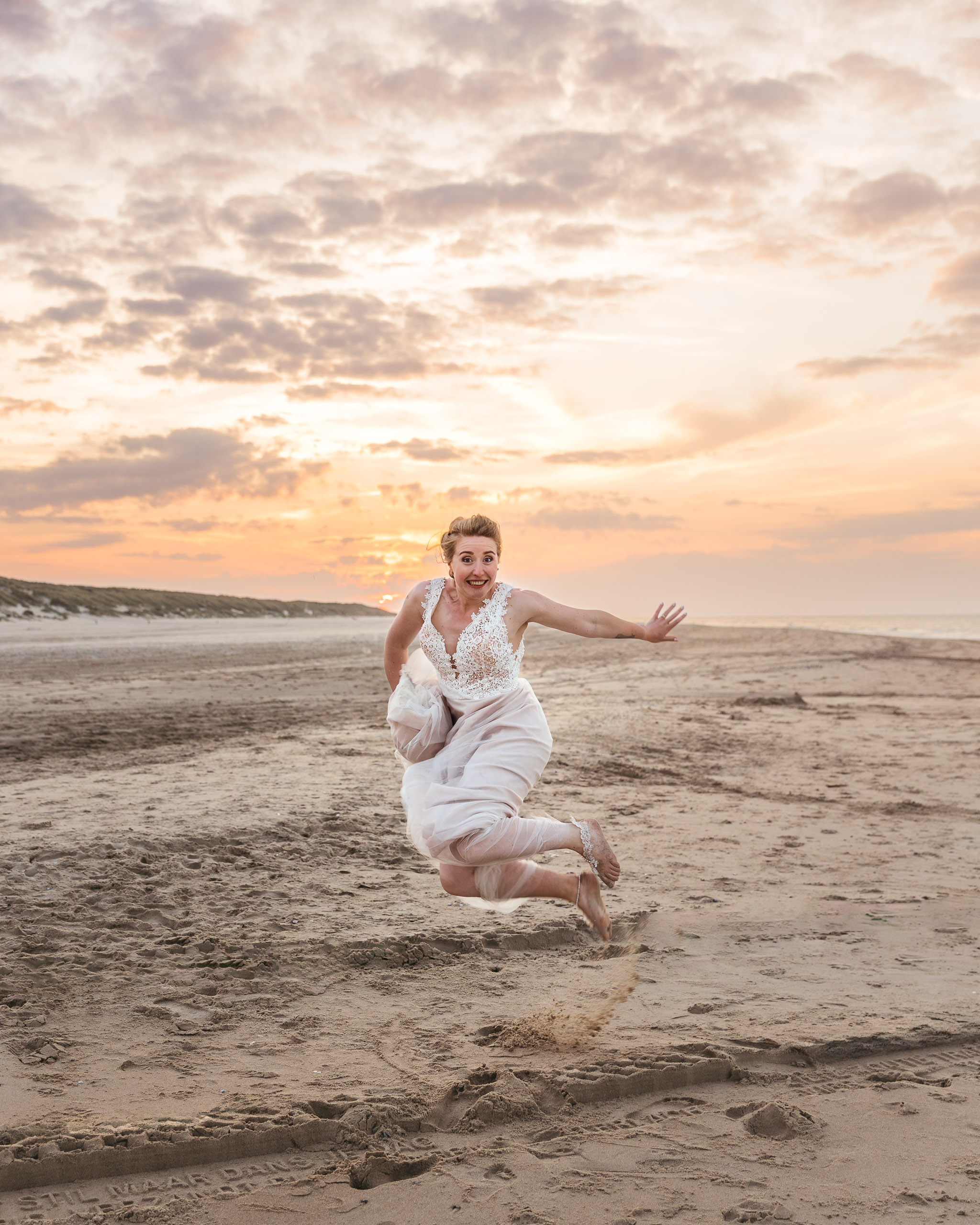 Een bruid die bij zonsondergang in de lucht springt op het strand tijdens een strandbruiloft op Vlieland.