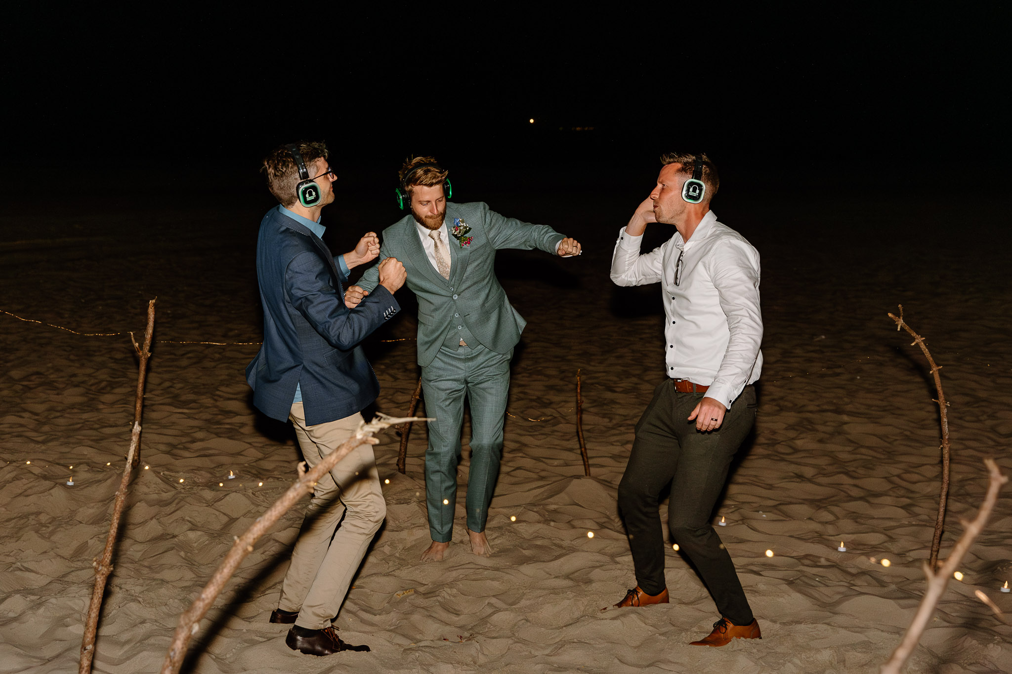 Drie mannen in pak dansen 's nachts op het strand tijdens een strandhuwelijksceremonie op Vlieland.