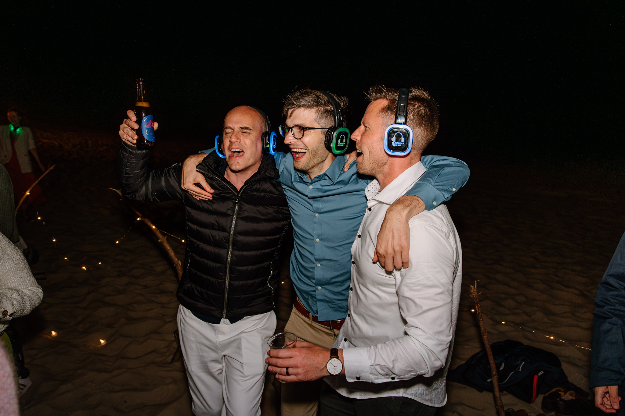 Een groep mannen op een strandfeest met koptelefoon op, genietend van een levendig trouwen op Vlieland-feest.