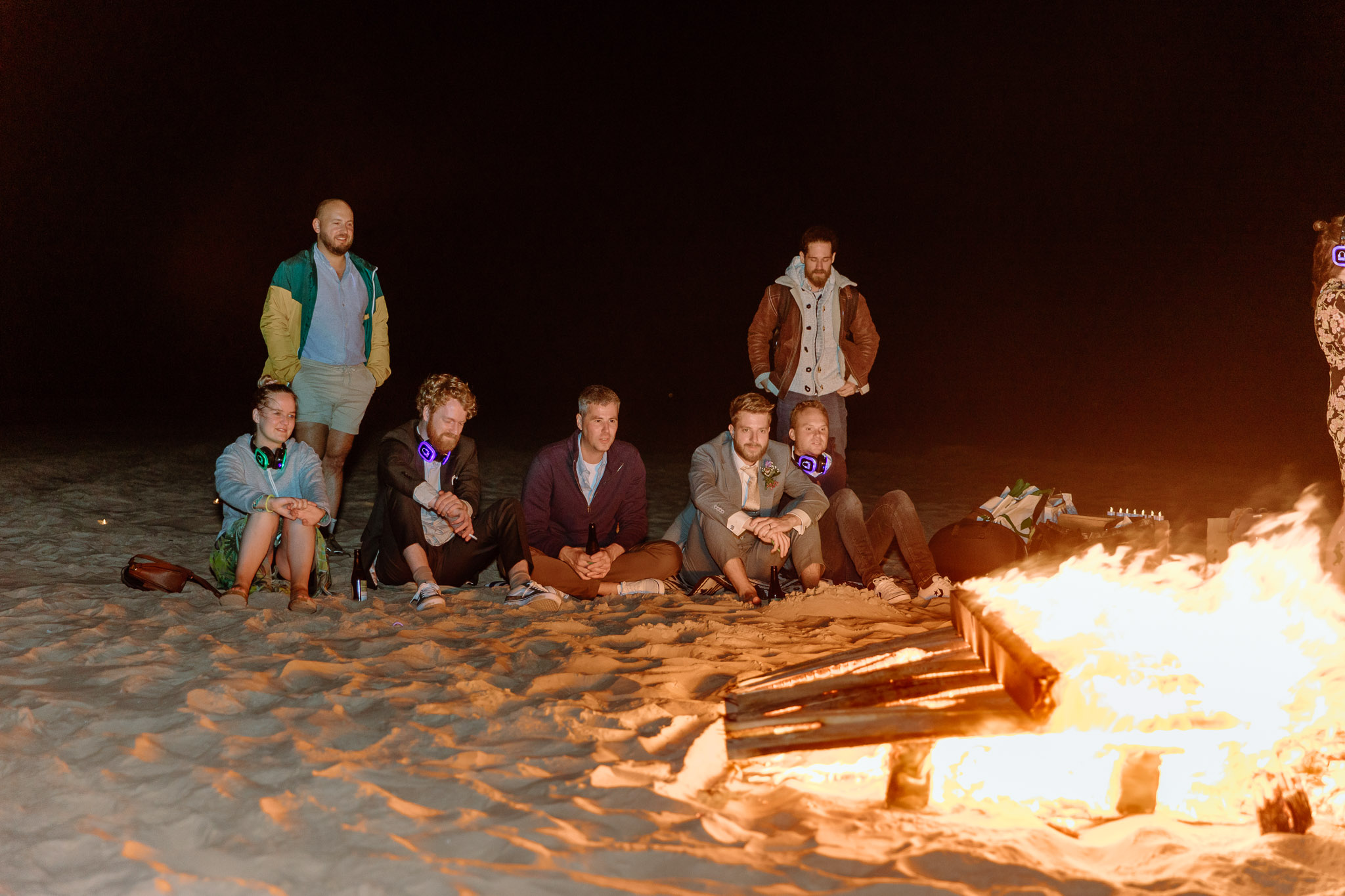 Een groep mensen zit rond een kampvuur op het strand van Vlieland en geniet van een strandhuwelijksfeest.