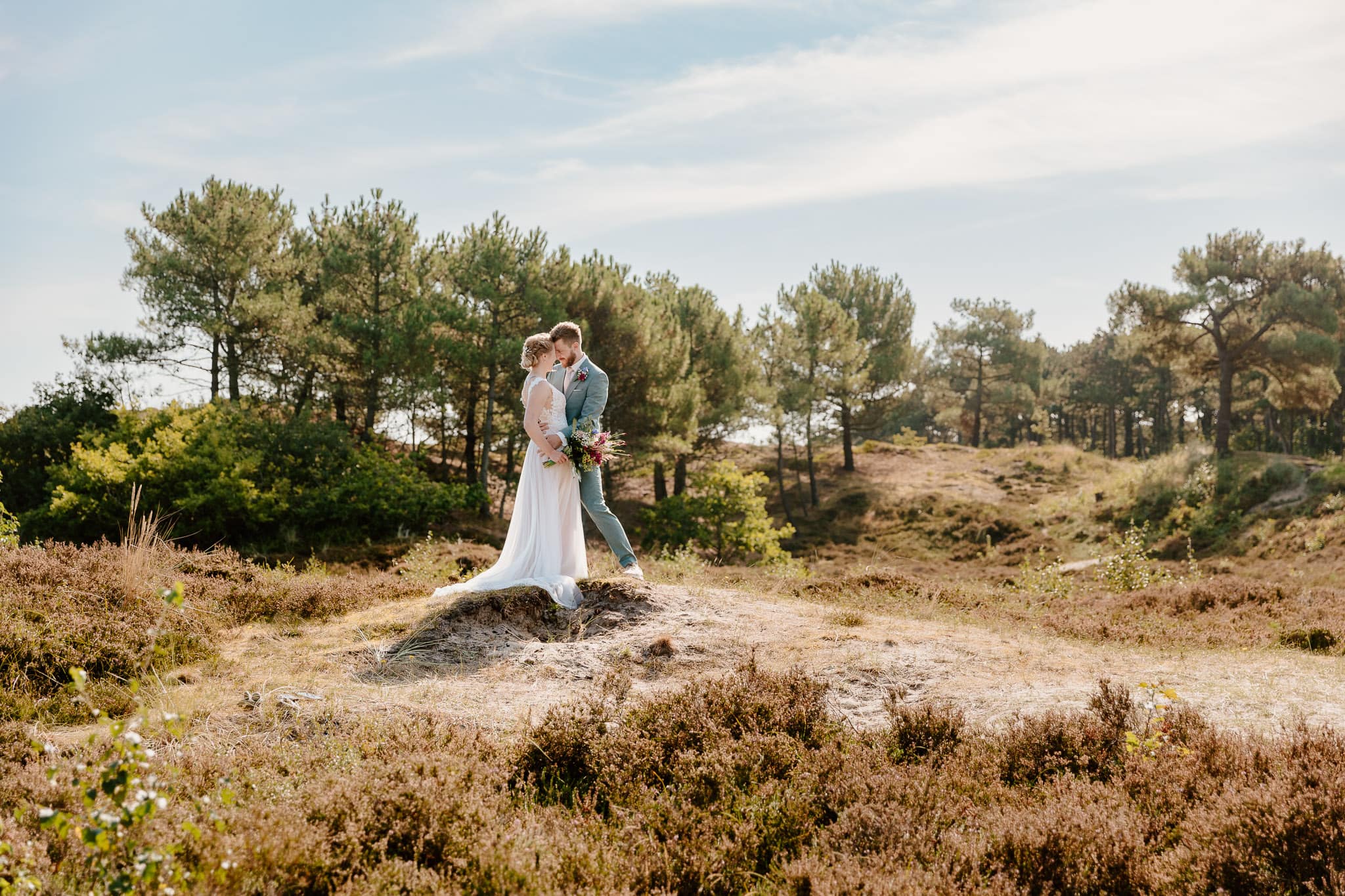 Trouwen op Vlieland - Een bruid en bruidegom staan op een rots in een veld.