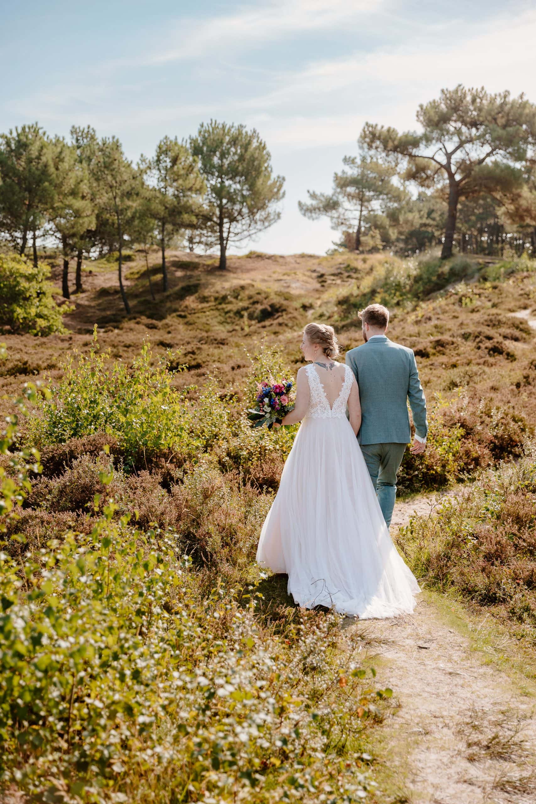 Trouwen op Vlieland - Een bruid en bruidegom die op hun speciale dag over een bospad lopen.