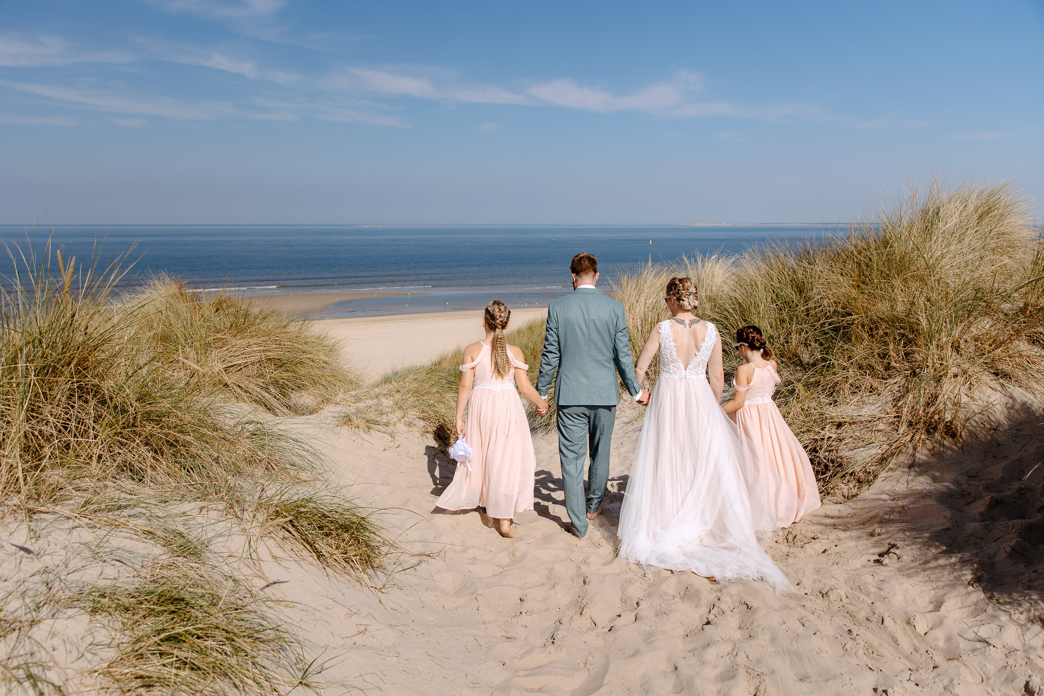 Een bruid en haar bruidsmeisjes lopen over een zandduin naar het strand voor hun strandbruiloft op Vlieland.