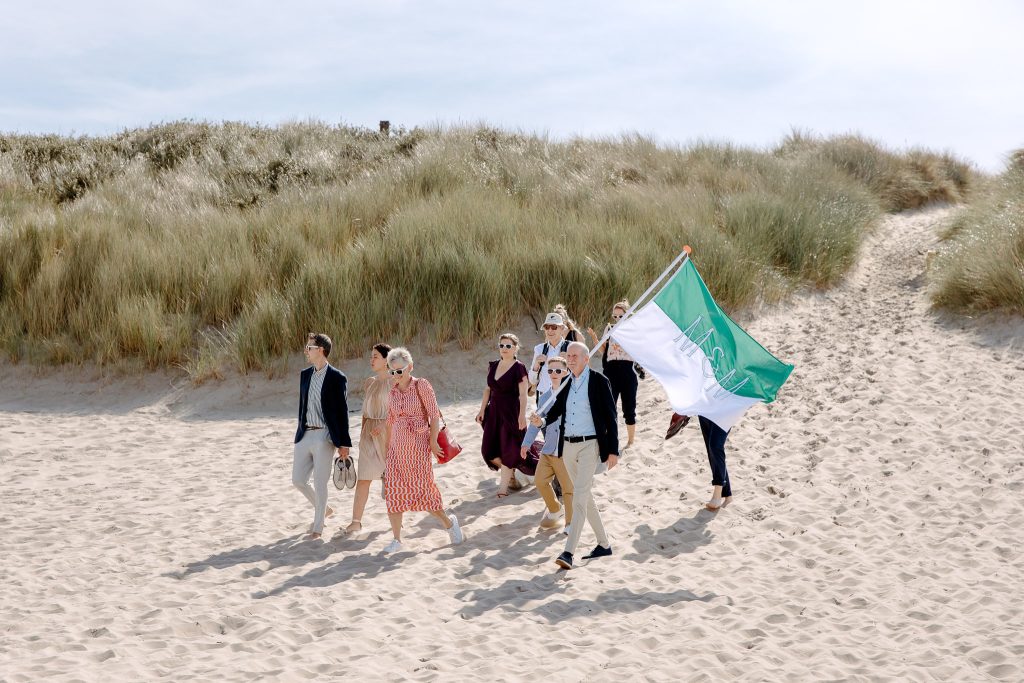 Een groep mensen die met een vlag over een strand lopen tijdens een strandbruiloft op Vlieland.