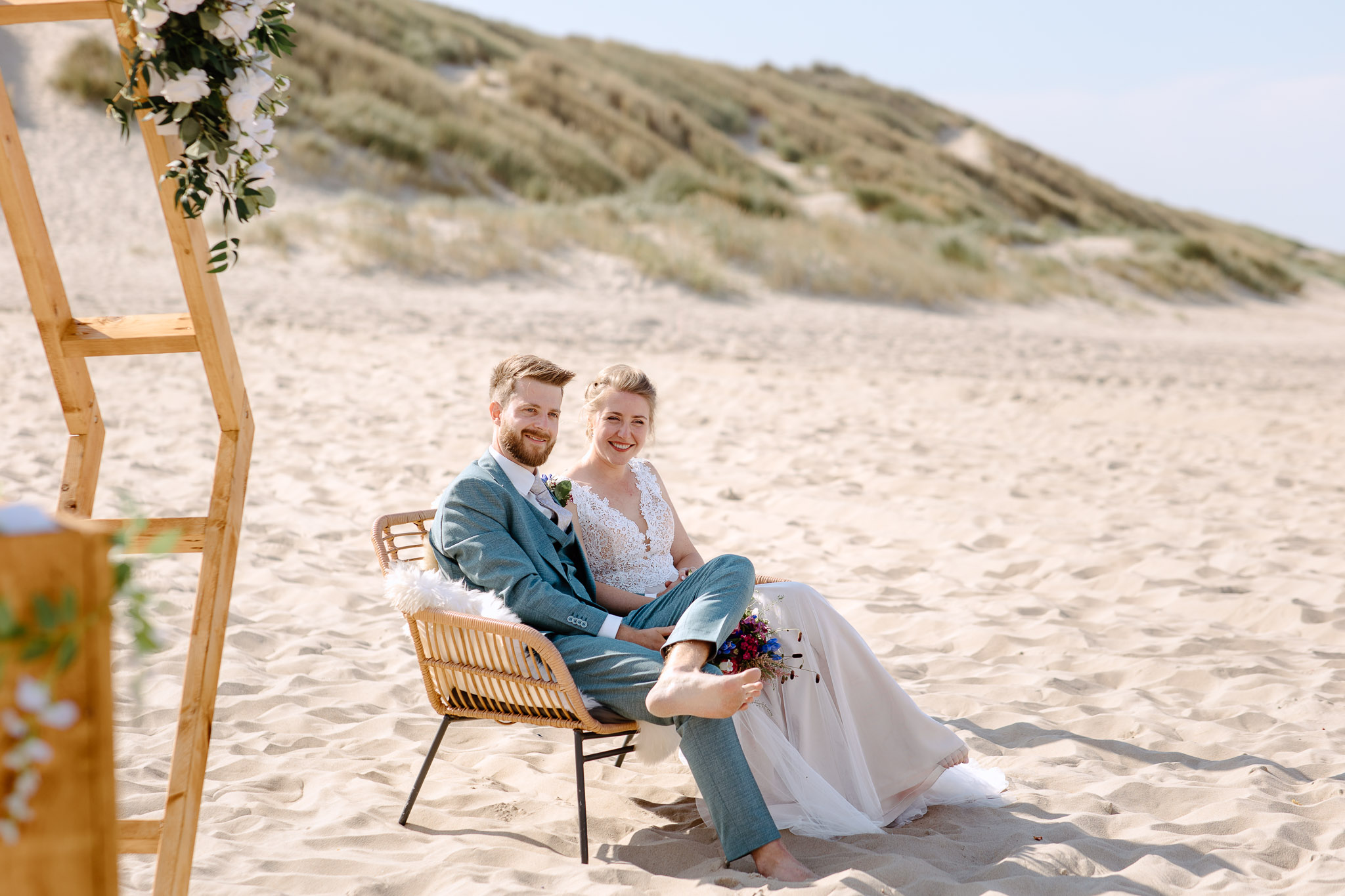 Een bruid en bruidegom zittend in stoelen op het strand tijdens hun strandbruiloft op Vlieland.