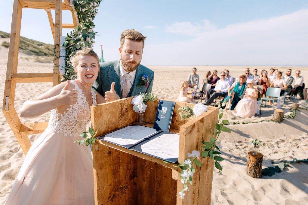 Een bruidspaar steekt de duim op na het ondertekenen van de trouwakte tijdens een strandbruiloft op Vlieland.