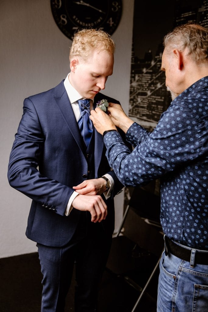 Bruidegom trekt zijn trouwpak aan en zijn vader helpt bij het opspelden van de corsage in Zwolle.