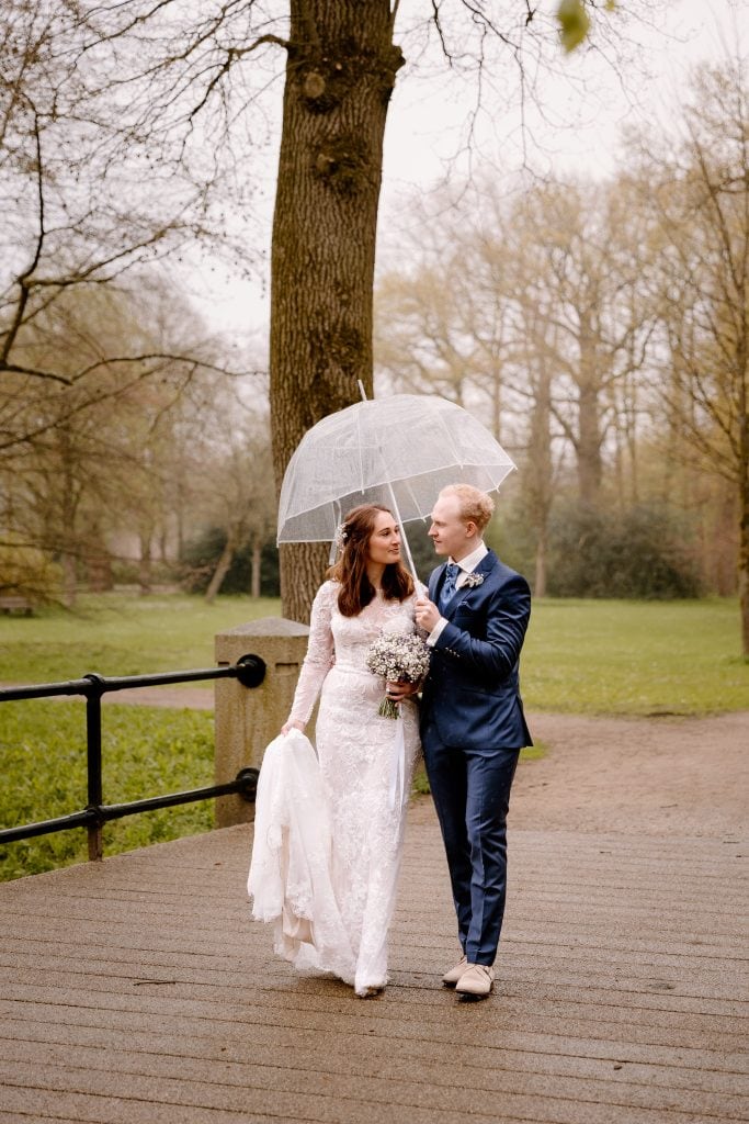 Een bruid en een bruidegom lopen tijdens de trouwfoto's onder een paraplu in Het Engelse Werk.