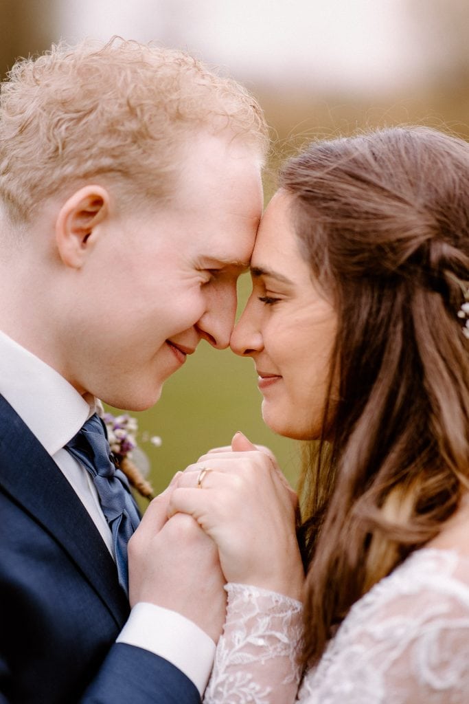 Een bruid en bruidegom houden hun voorhoofd tegen elkaar en elkaars handen vast tijdens de fotoshoot op hun bruiloft.