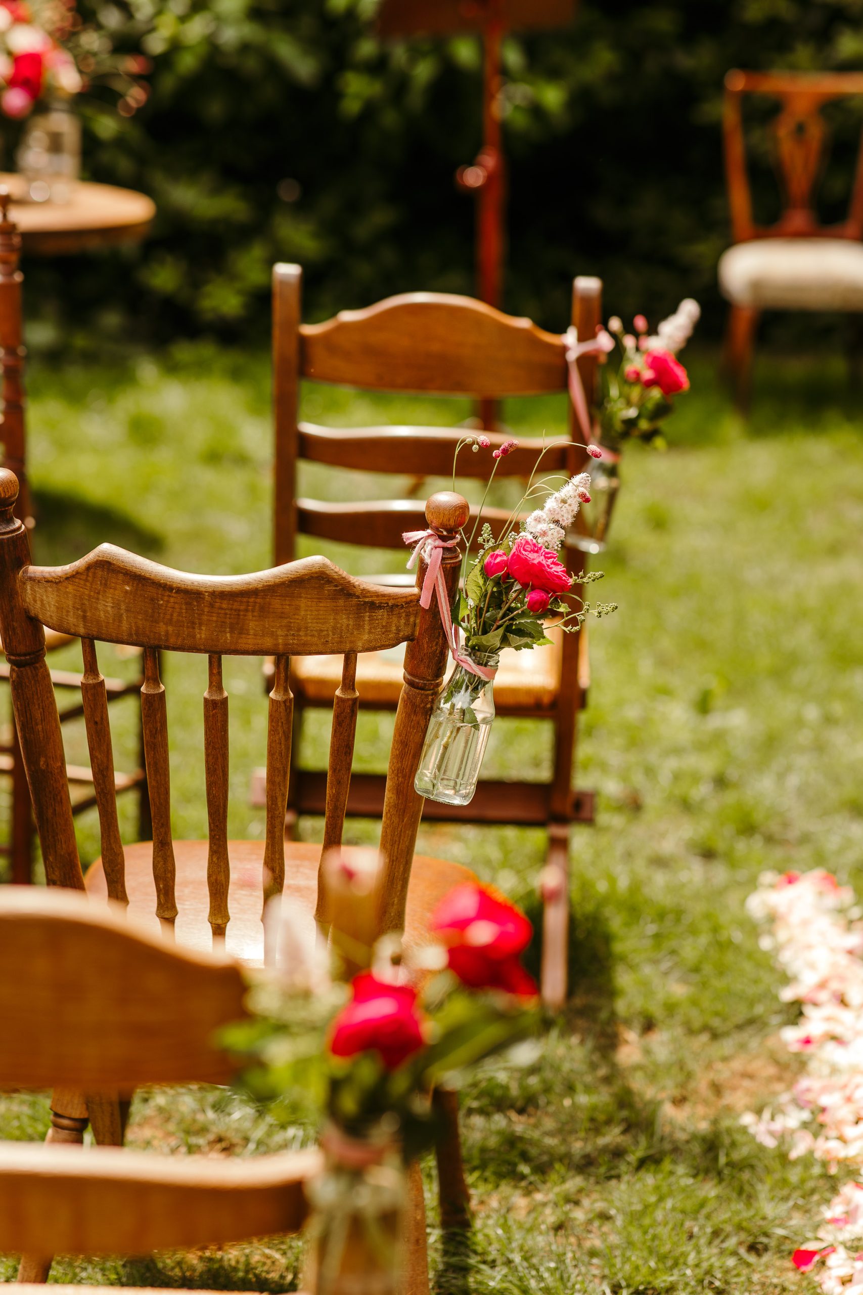 Vaasjes met daarin mooie roze bloemen die hangen aan de stoelen langs het gangpad waarover de bruid en bruidegom komen aanlopen tijdens hun bruiloft in Friesland.