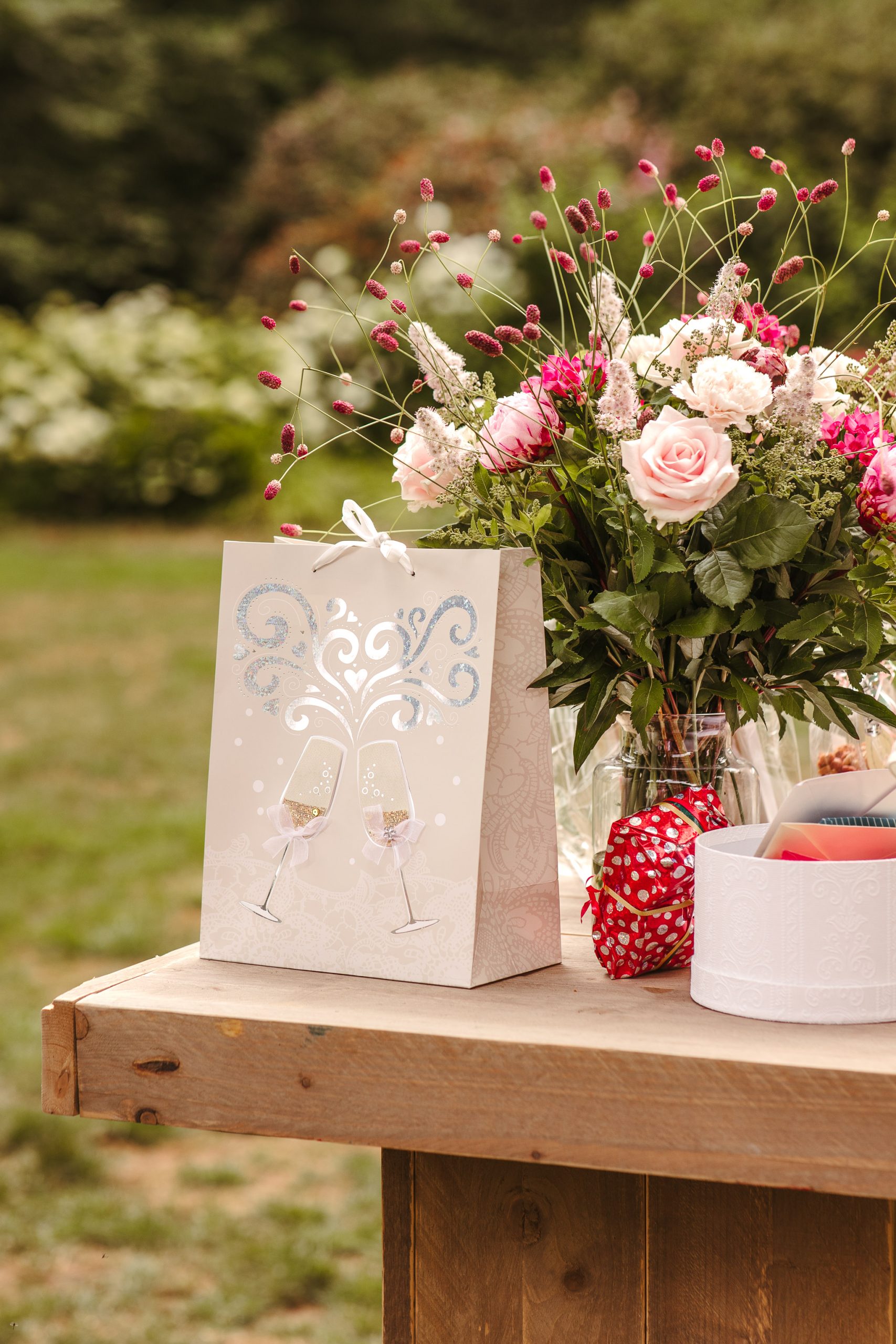 Een decoratief cadeauzakje met champagneglazen staat op de cadeautafel naast een groot boeket roze rozen tijdens een bruiloft in Friesland.