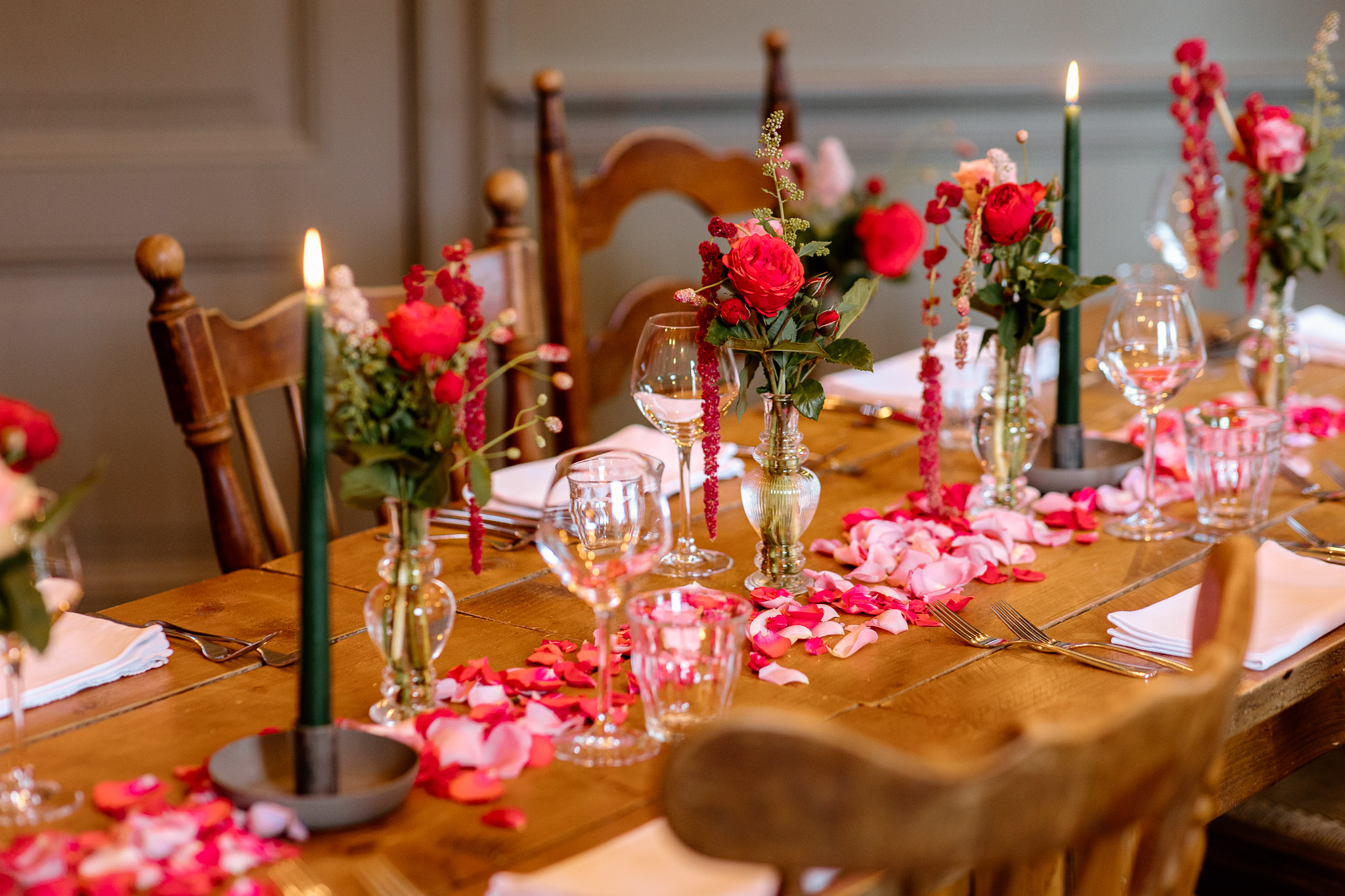 Een prachtig gedekte eettafel, gedecoreerd met rozenblaadjes, groene kaarsen en vazen met rode en roze bloemen, helemaal klaar voor het diner tijdens de bruiloft.