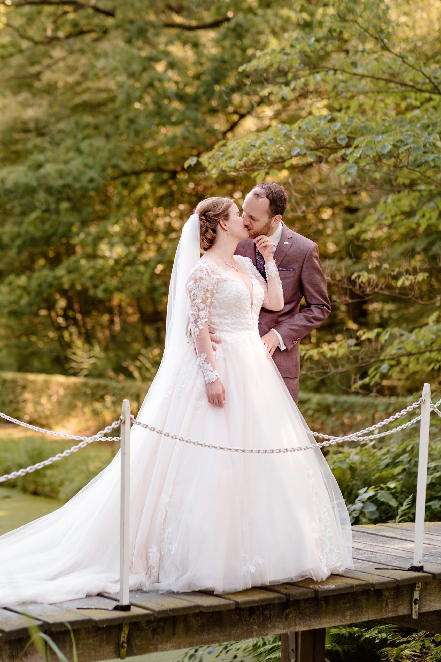 Een bruidspaar geeft elkaar een kus op een bruggetje tijdens het maken van hun trouwfoto's in Friesland, voordat ze gaan trouwen bij de Slotplaats in Bakkeveen.