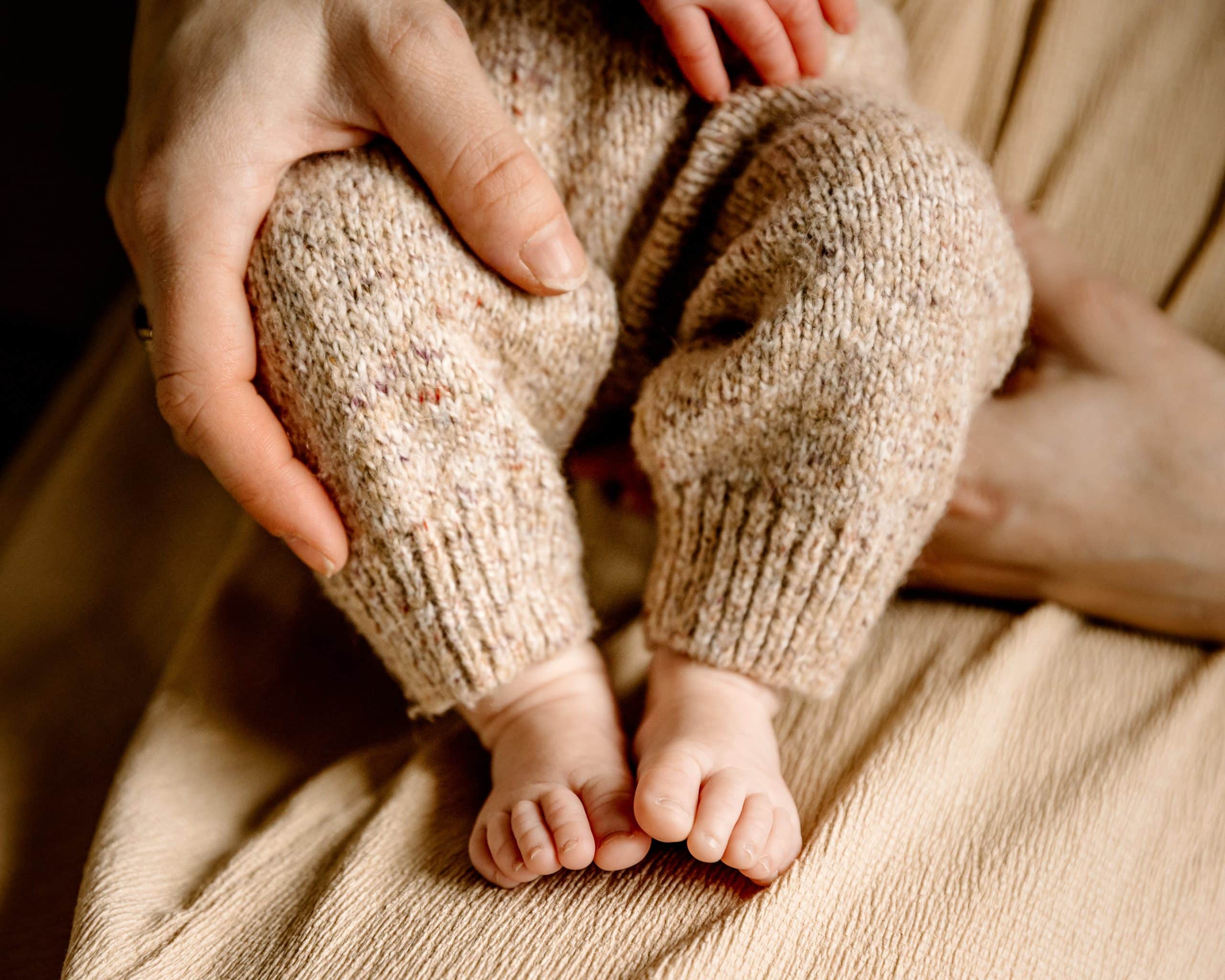 Fotograaf gezin en newborn legt een nieuwe moeder vast die de voetjes van haar pasgeboren baby vasthoudt.