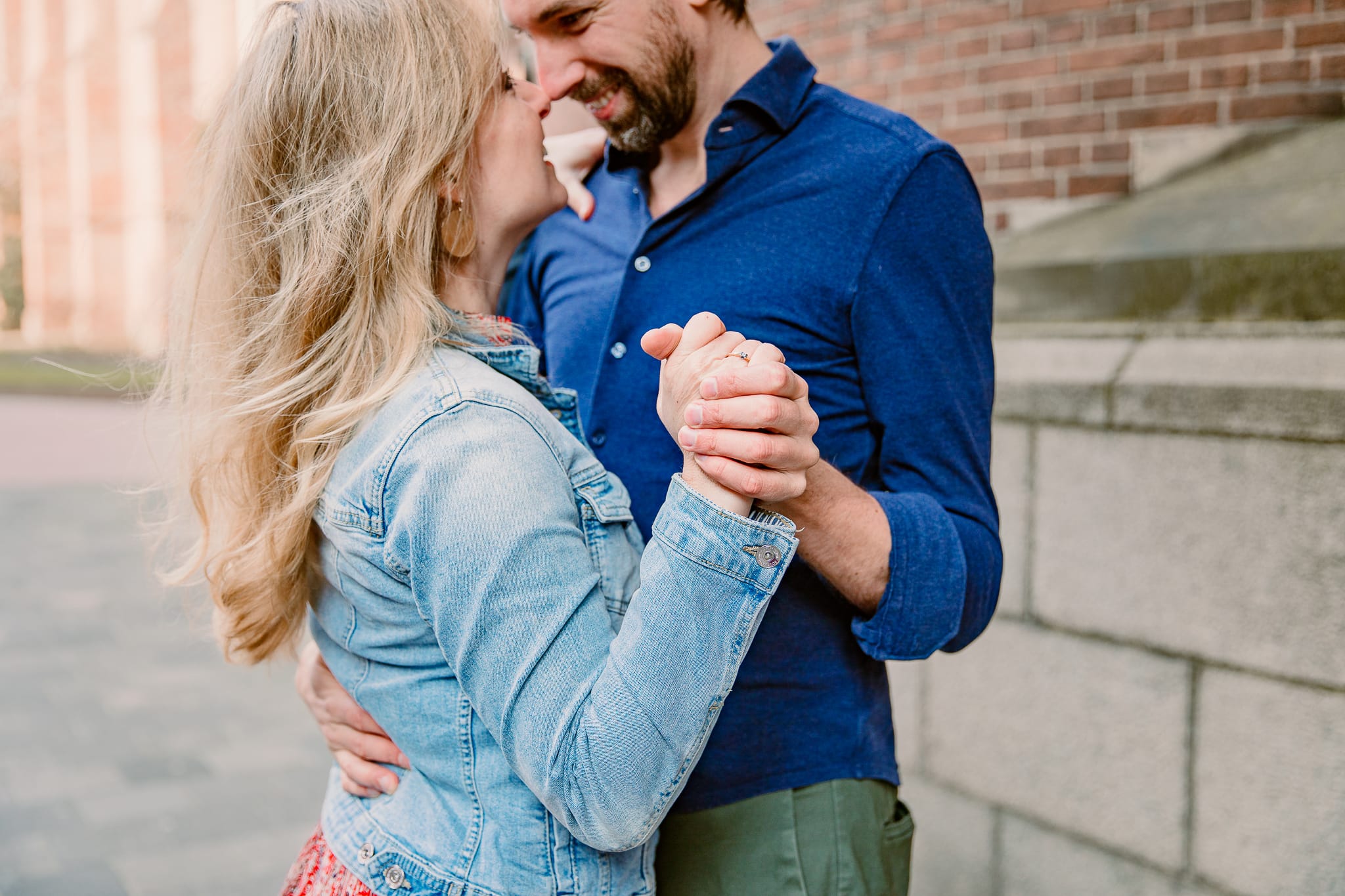 Verloofd stel in spijkerjasje en blauwe blouse staat in stijldanshouding en houden hun voorhoofden tegen elkaar voor de Martinikerk in Groningen tijdens een loveshoot..