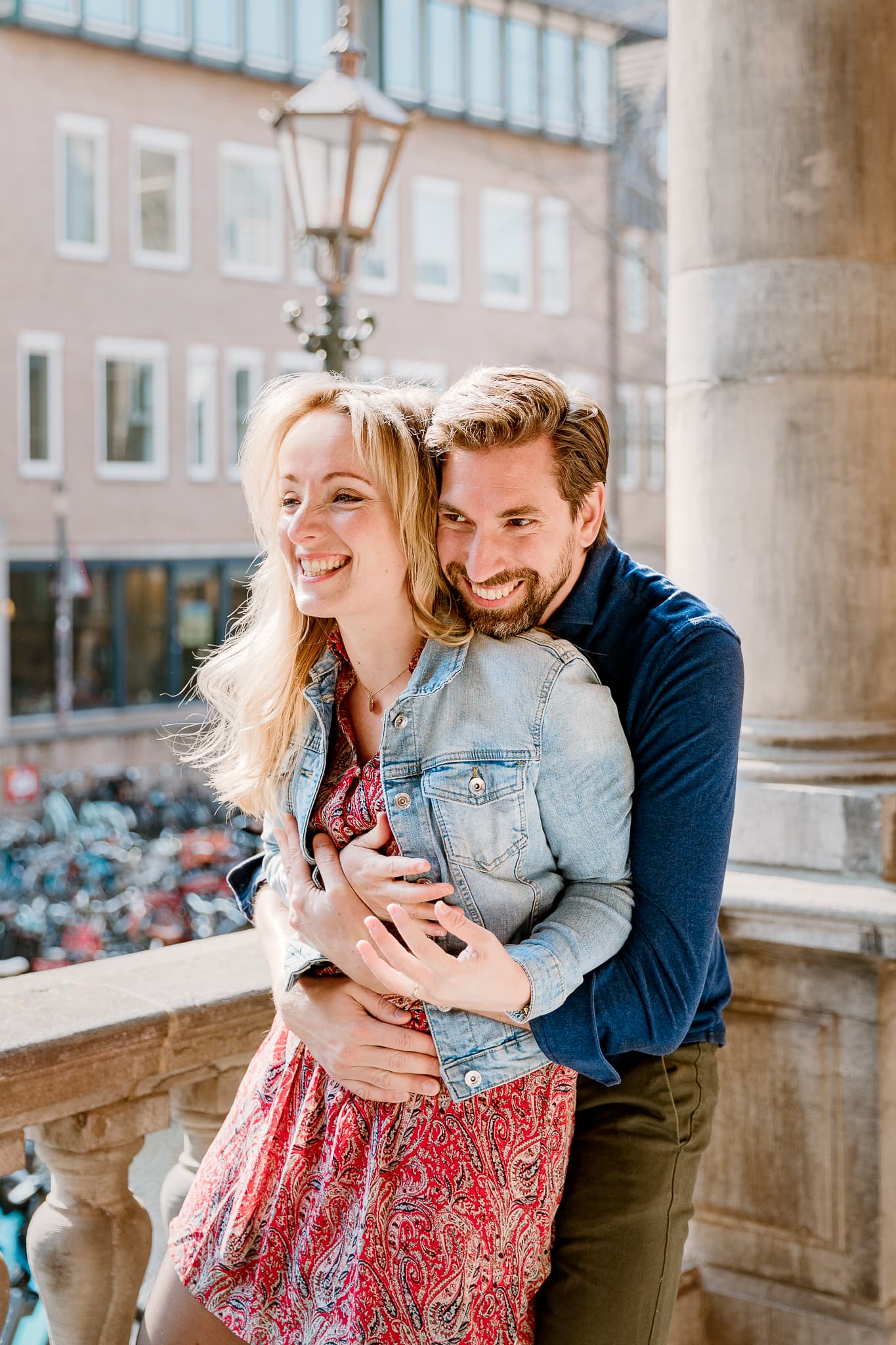 Man laat zijn verloofde van achteren schrikken terwijl ze beide lachen voor de ingang van het Academiegebouw van de Rijksuniversiteit Groningen