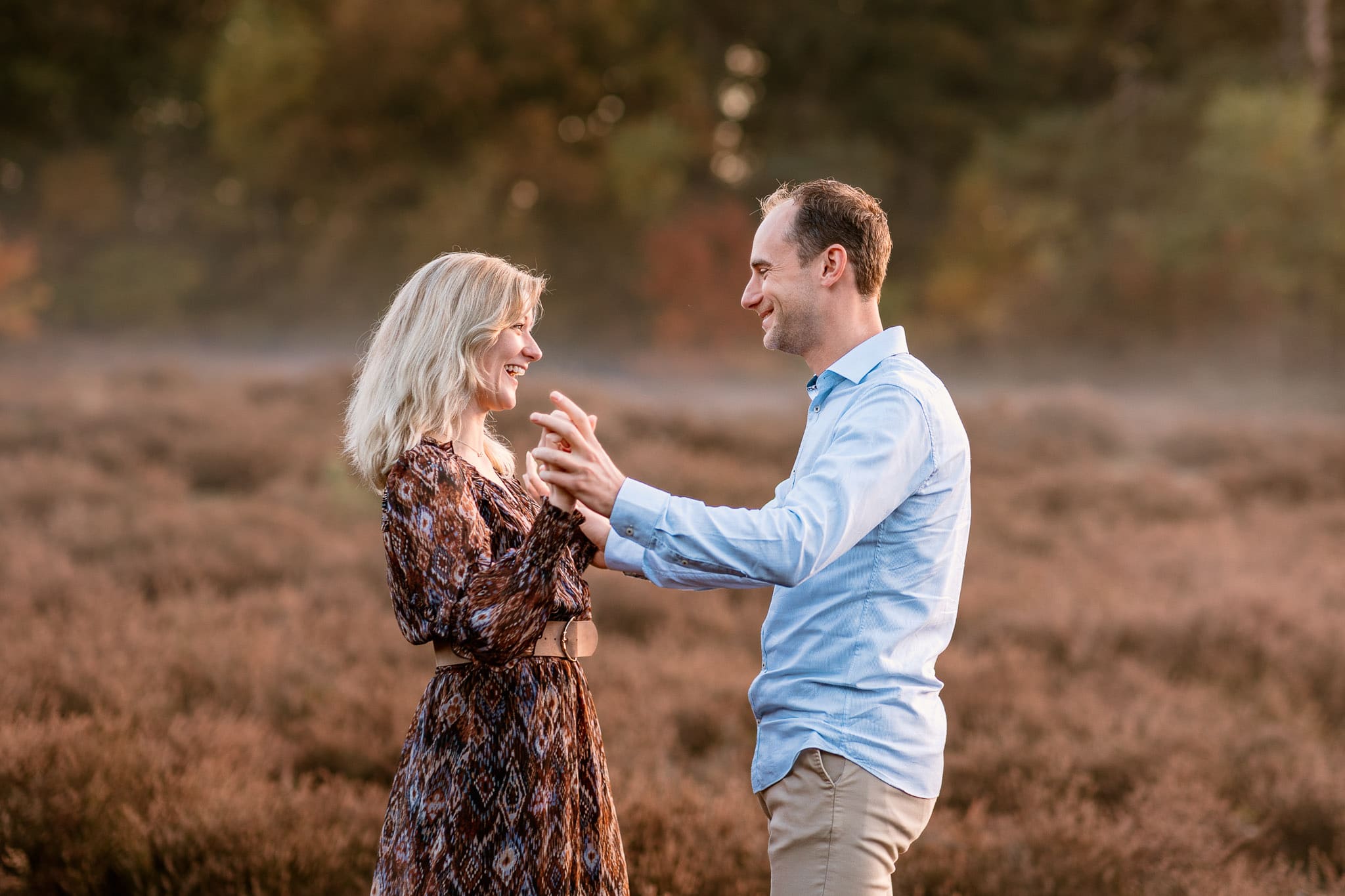 Stel houdt elkaars handen vast en kijkt elkaar lachend aan tijdens een loveshoot op de heide in Drenthe