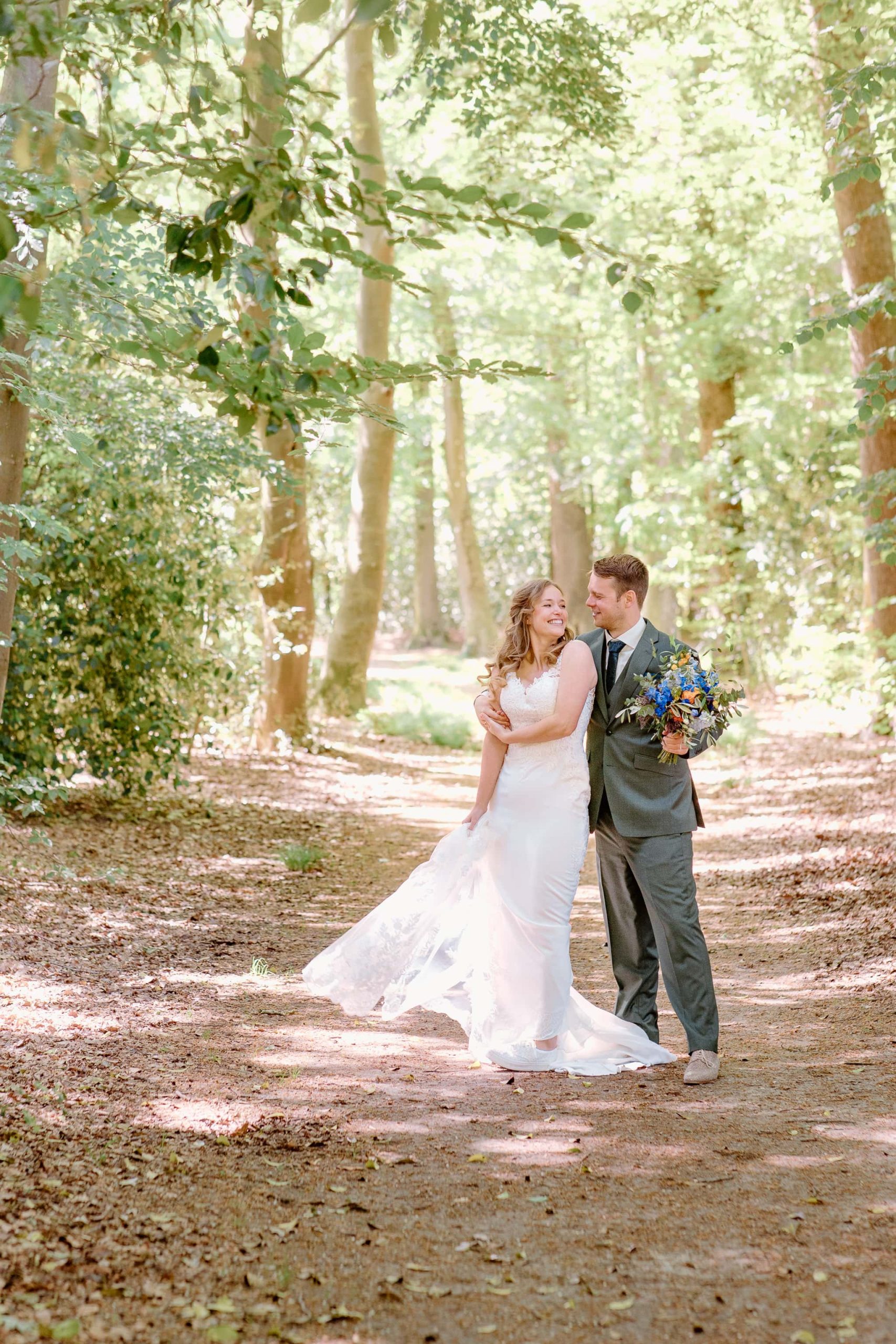 Een foto van een bruidspaar in het bos bewerkt in light and airy trouwfotografie stijl.