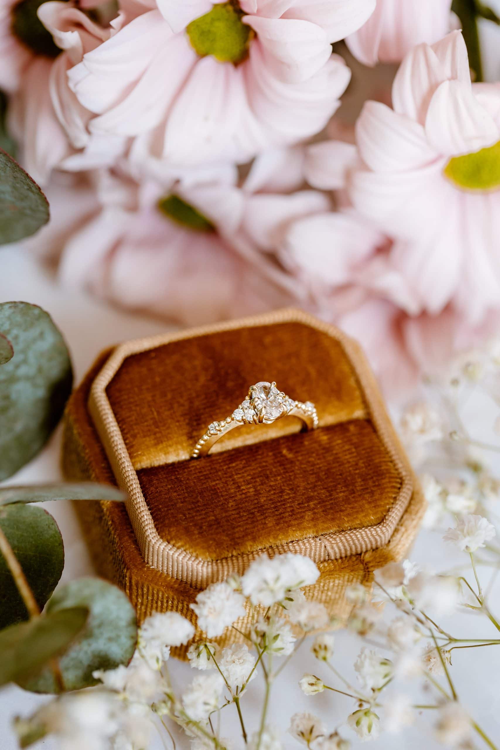 Een detailfoto van een verlovingsring omringd door bloemen.